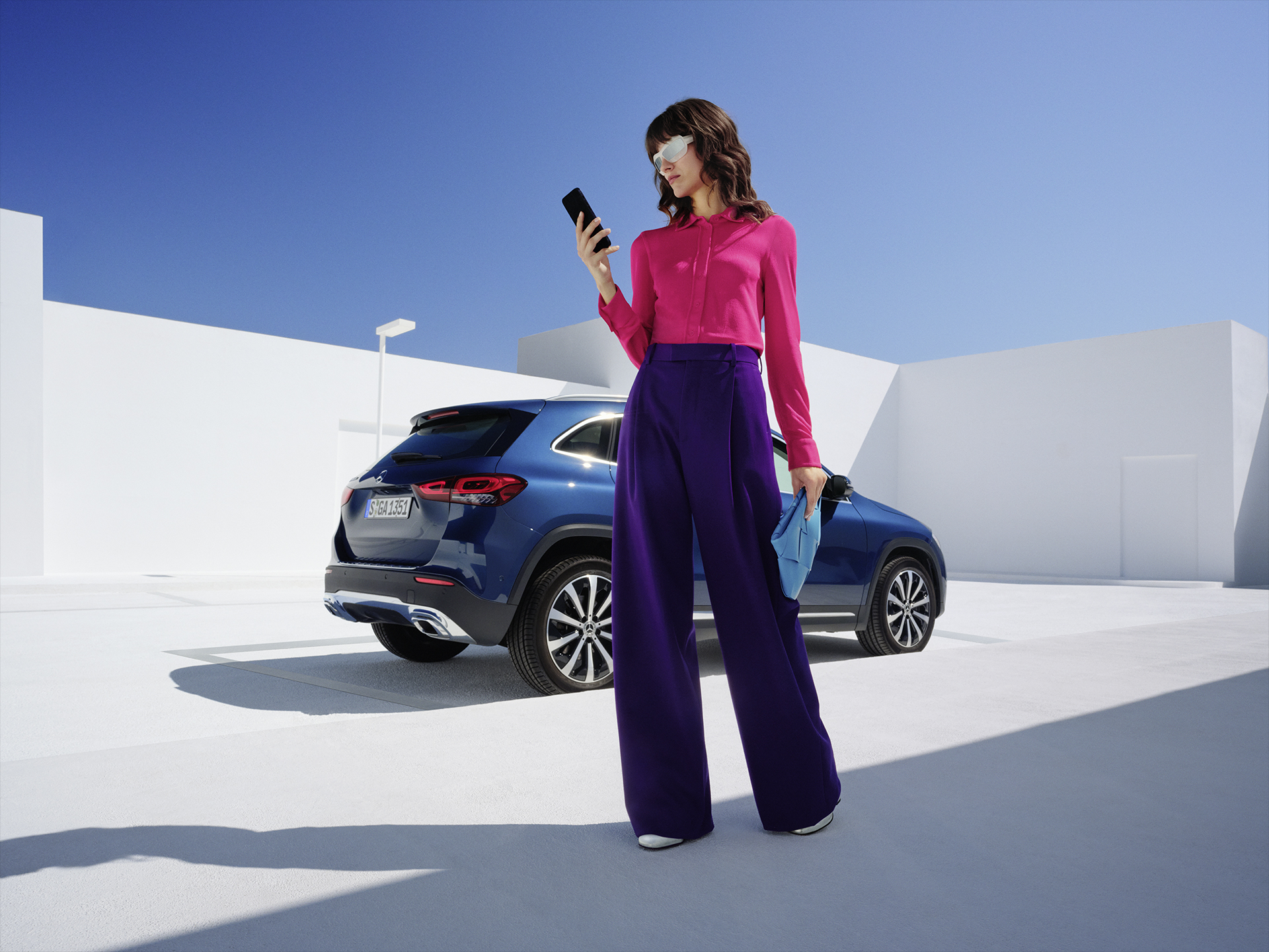 Mercedes me ID | Digital extras | Mercedes-Benz Una donna è in piedi davanti a una Mercedes-Benz GLA e guarda il suo telefono.
