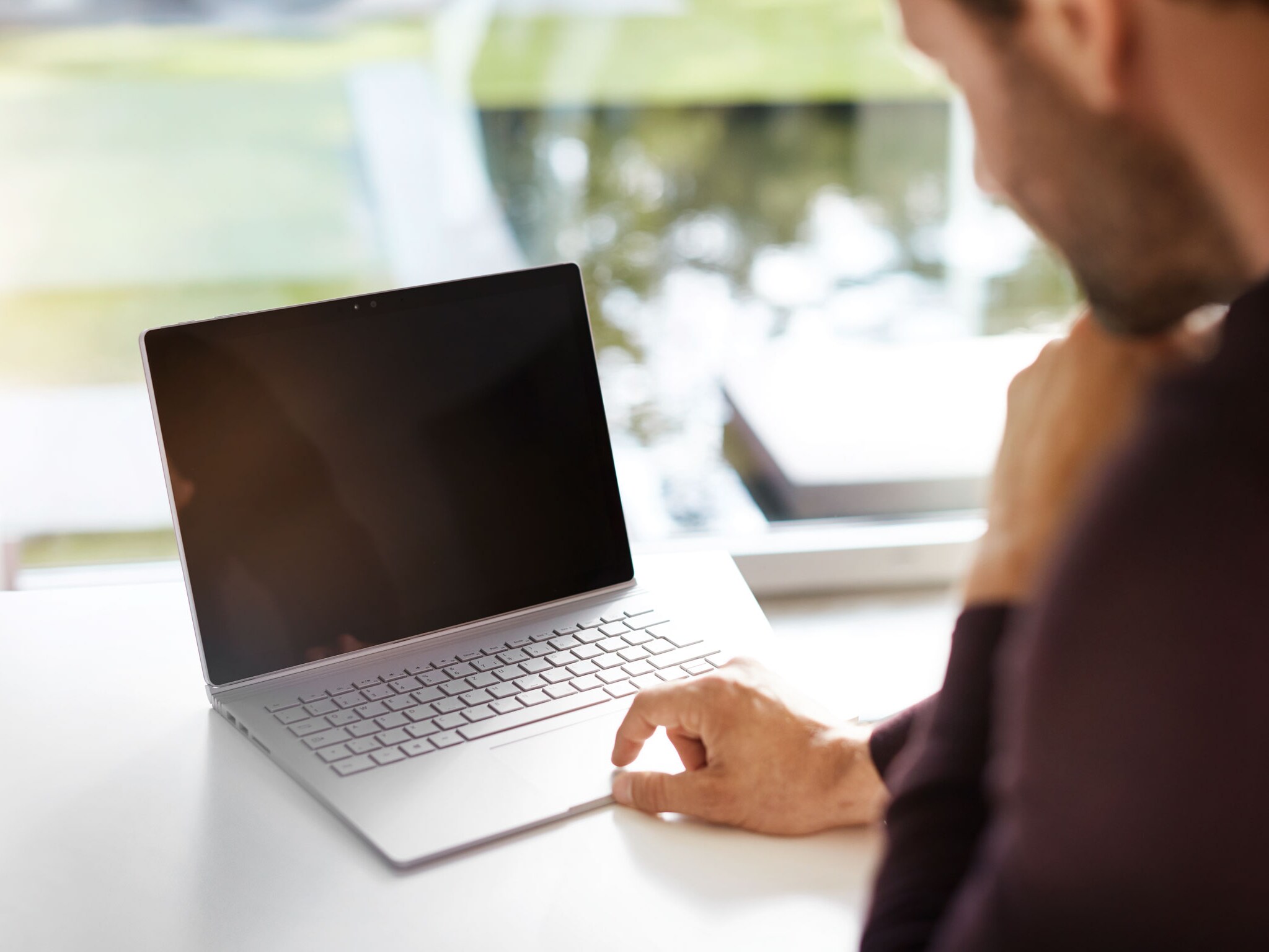 Un primo piano di un computer portatile su una scrivania con una persona che si avvicina ad esso