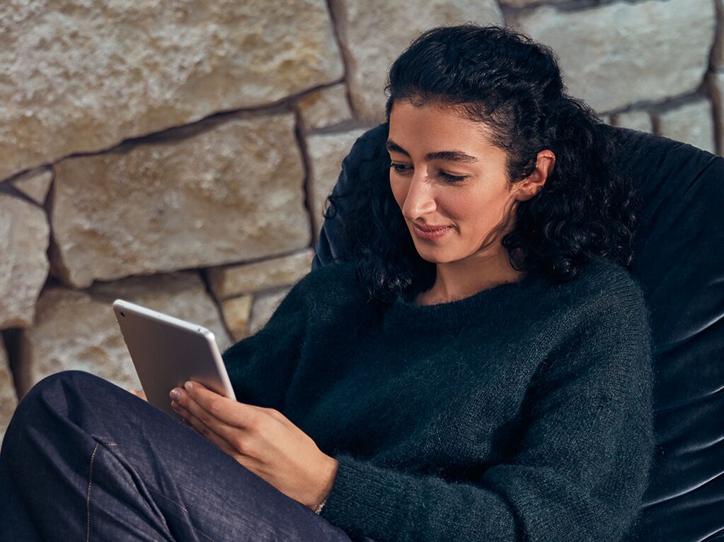 Una persona mentre si rilassa con un tablet su una sedia di fronte a un muro di pietra