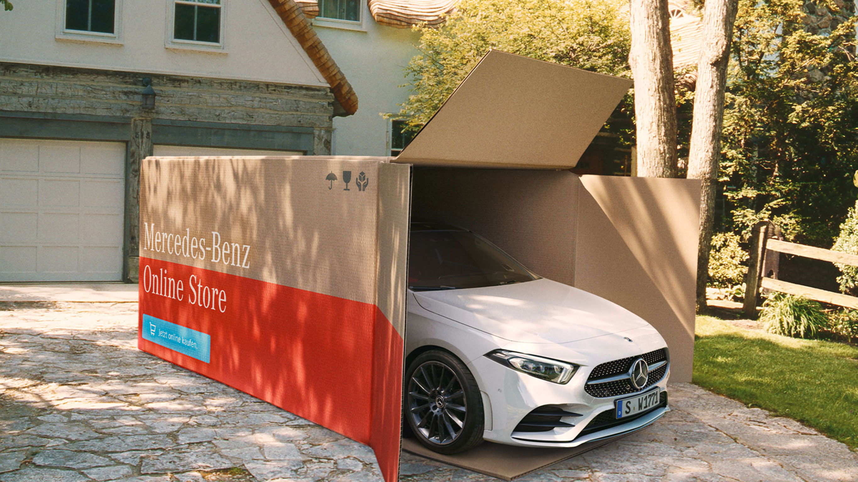 Scopri l'esperienza del Mercedes-Benz Online Store Un veicolo Mercedes-Benz parzialmente scoperto in una grande scatola di cartone con la scritta "Mercedes-Benz Online Store"