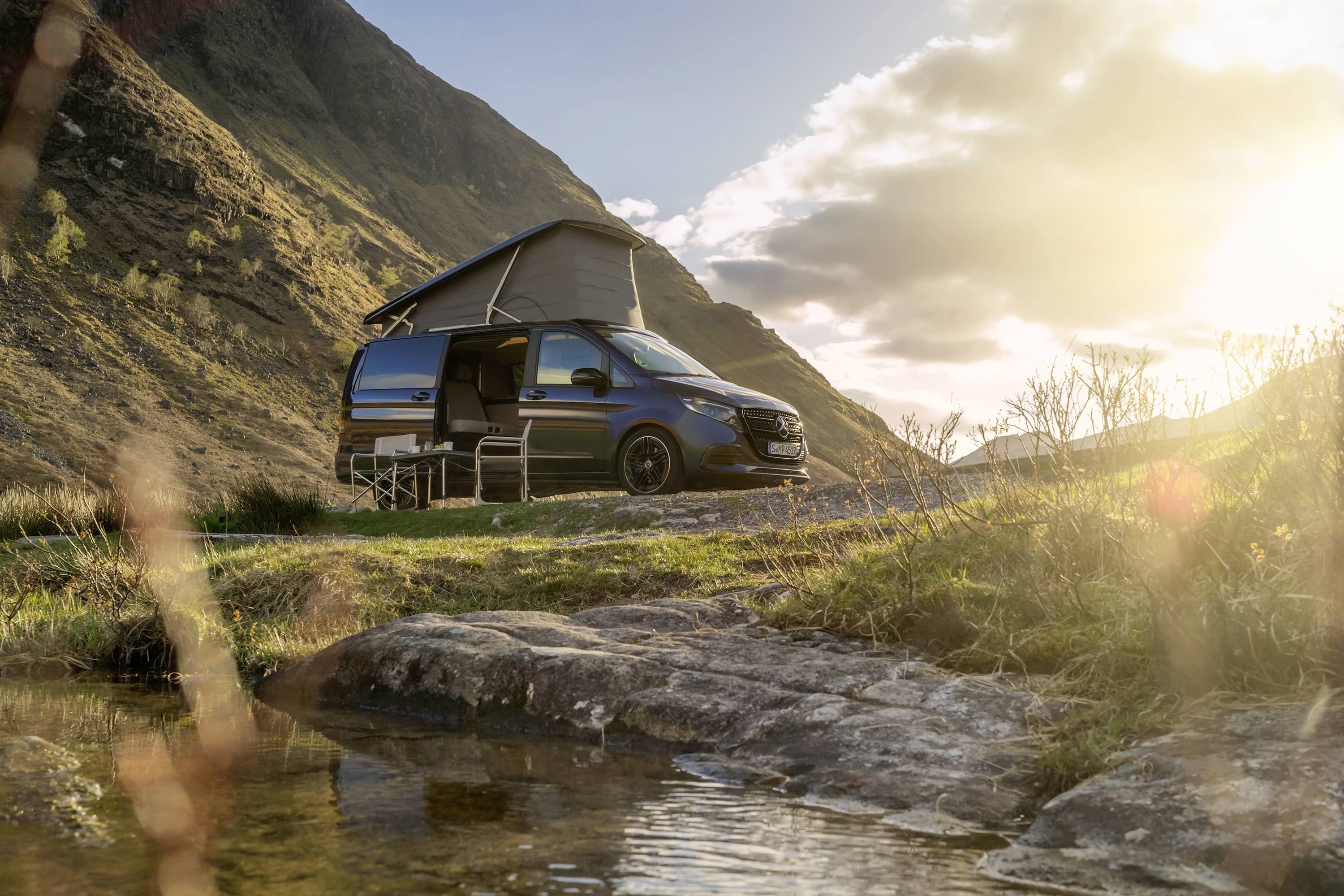 Marco Polo | Sprinter camper | Mercedes-Benz Un camper Mercedes-Benz Marco Polo con tetto a soffietto, immerso in un suggestivo paesaggio montano, che mette in risalto l’avventura all’aria aperta e la libertà della “vanlife”.