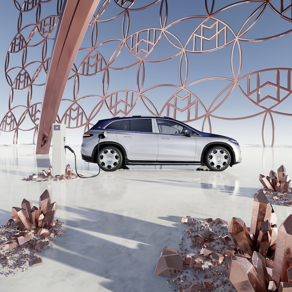 Vista laterale di Mercedes-Maybach EQS SUV alla stazione di ricarica, con il logo del Marchio Maybach sullo sfondo.