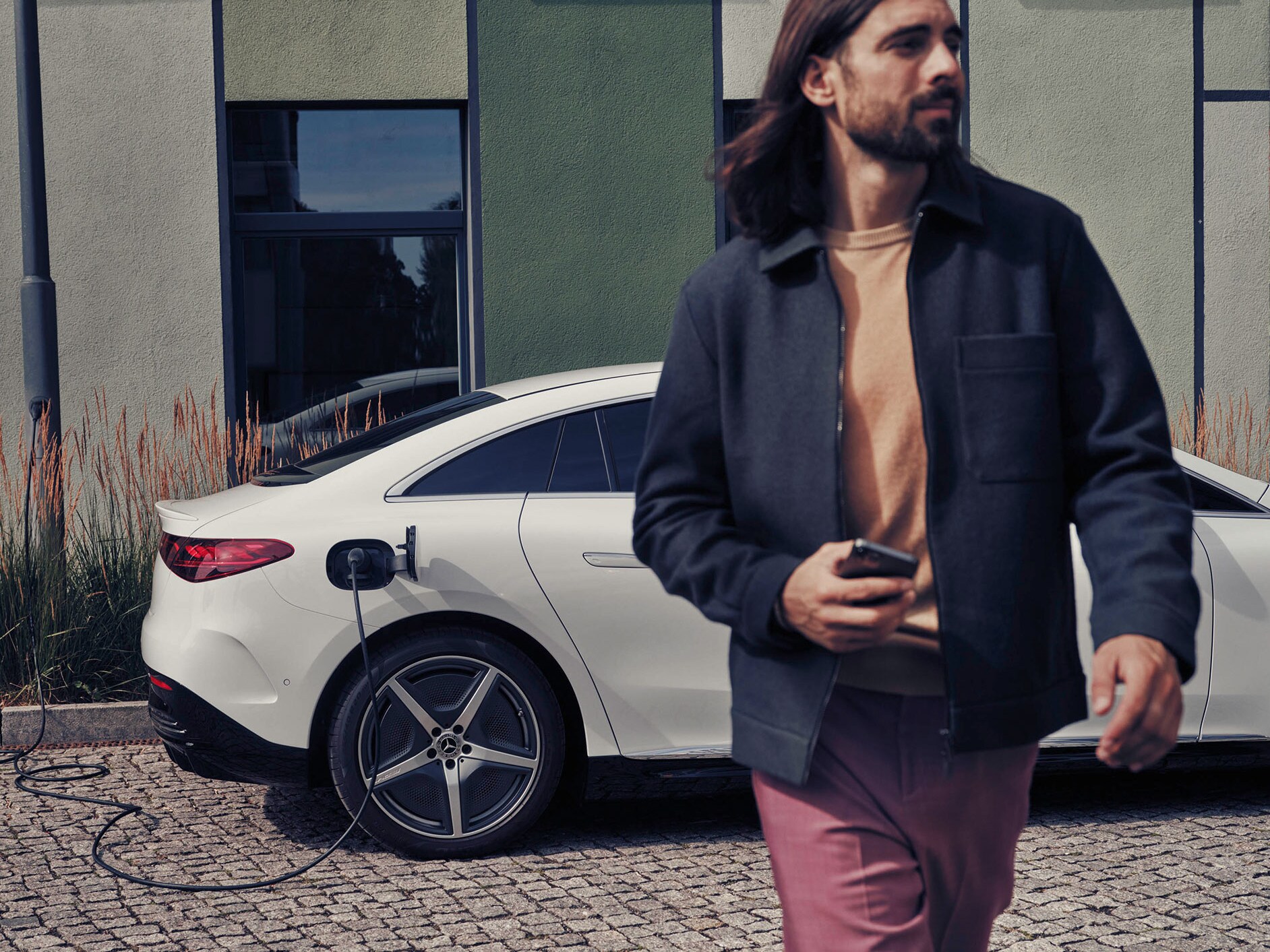 Man walking next to a charging white  Mercedes-Benz EQE