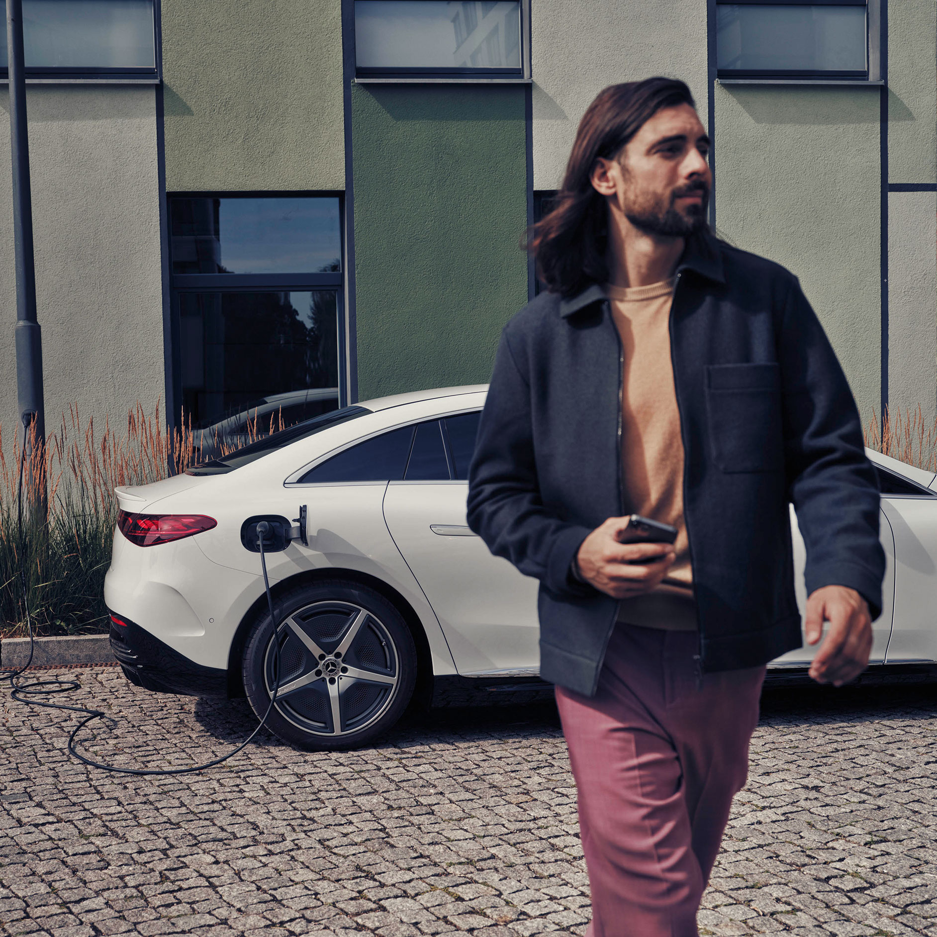Abbonamento | Financial Services | Mercedes-Benz Man walking next to a charging white Mercedes-Benz EQE