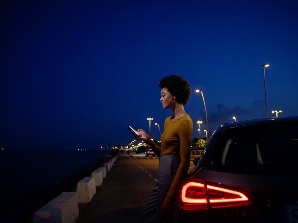 Donna appoggiata a una Mercedes-Benz con in mano uno smartphone