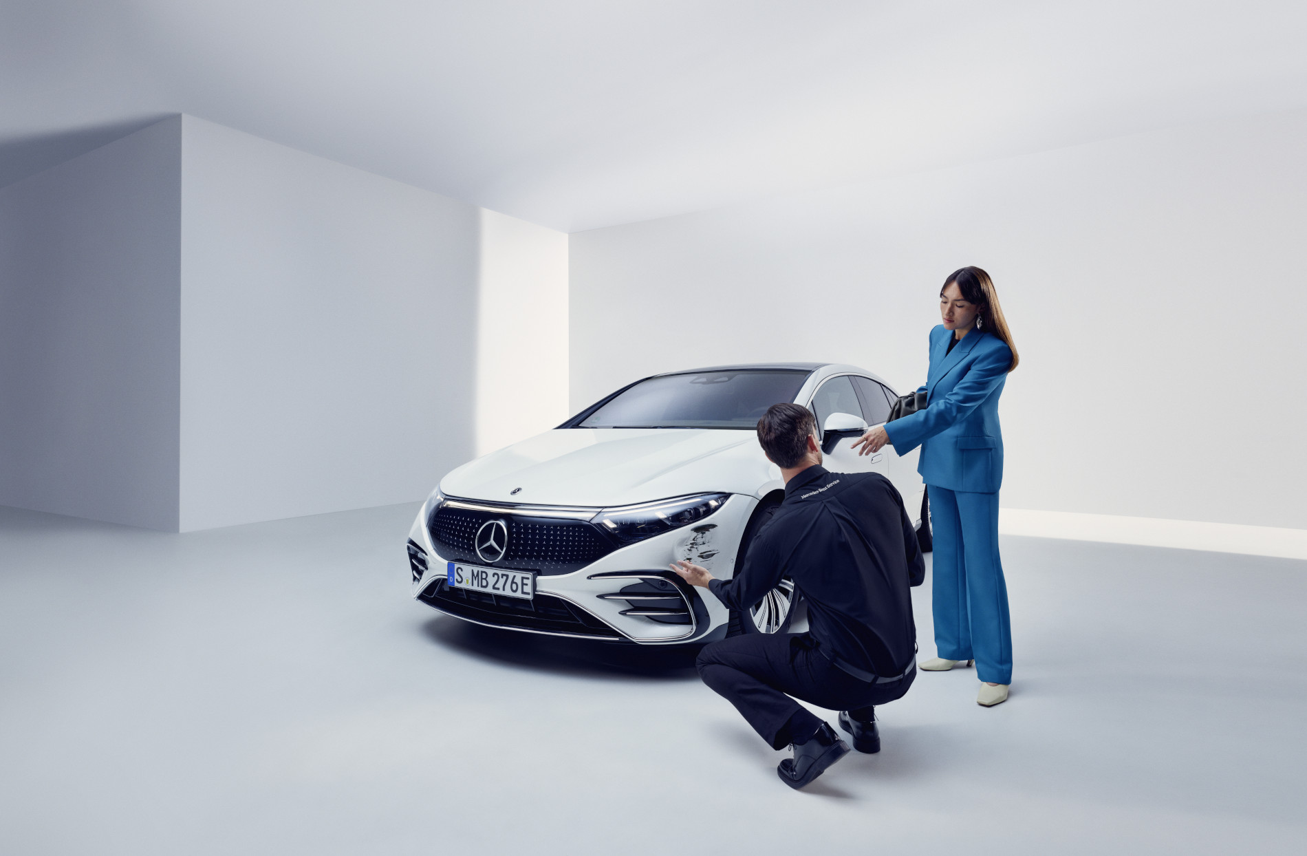 Riparazione danni | Mercedes-Benz Una persona del servizio assistenza Mercedes-Benz inginocchiato accanto a una Mercedes-Benz danneggiata.
