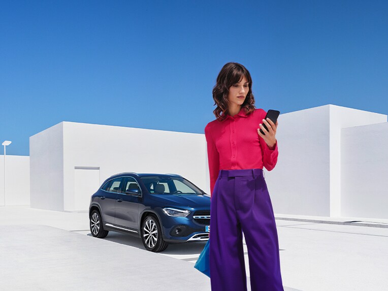 Una donna stabilisce un collegamento con la sua Mercedes-Benz tramite l'App Mercedes-Benz dal suo smartphone.