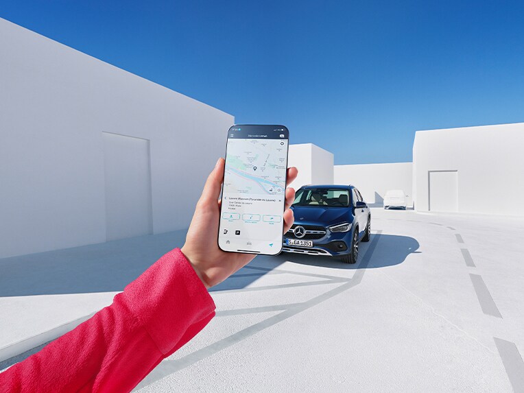 Qualcuno tiene in mano uno smartphone sul quale si vede l'App Mercedes-Benz Service. Sullo sfondo c'è un veicolo Mercedes-Benz.