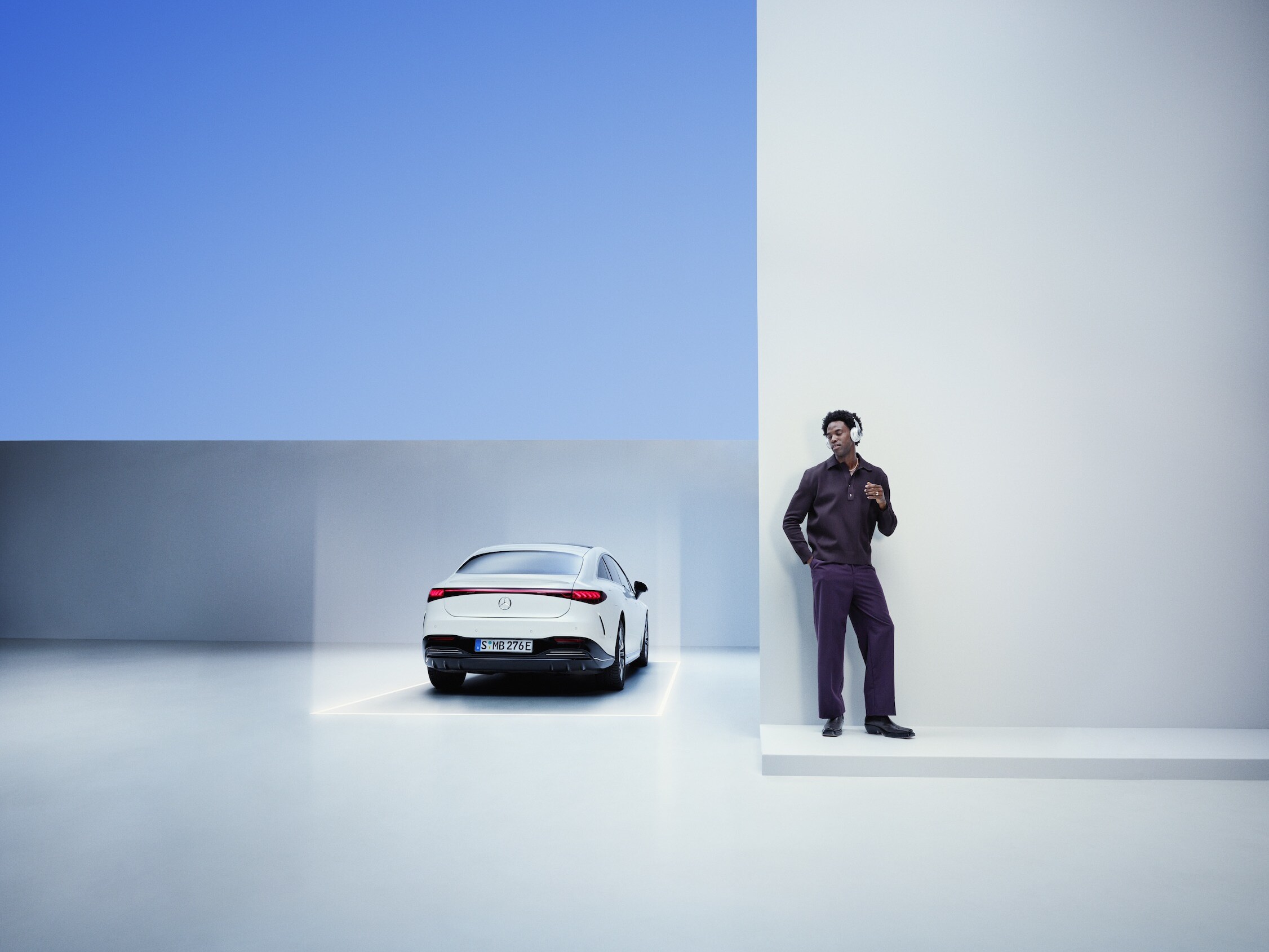 Un uomo con le cuffie si appoggia a un muro accanto alla sua Mercedes-Benz.