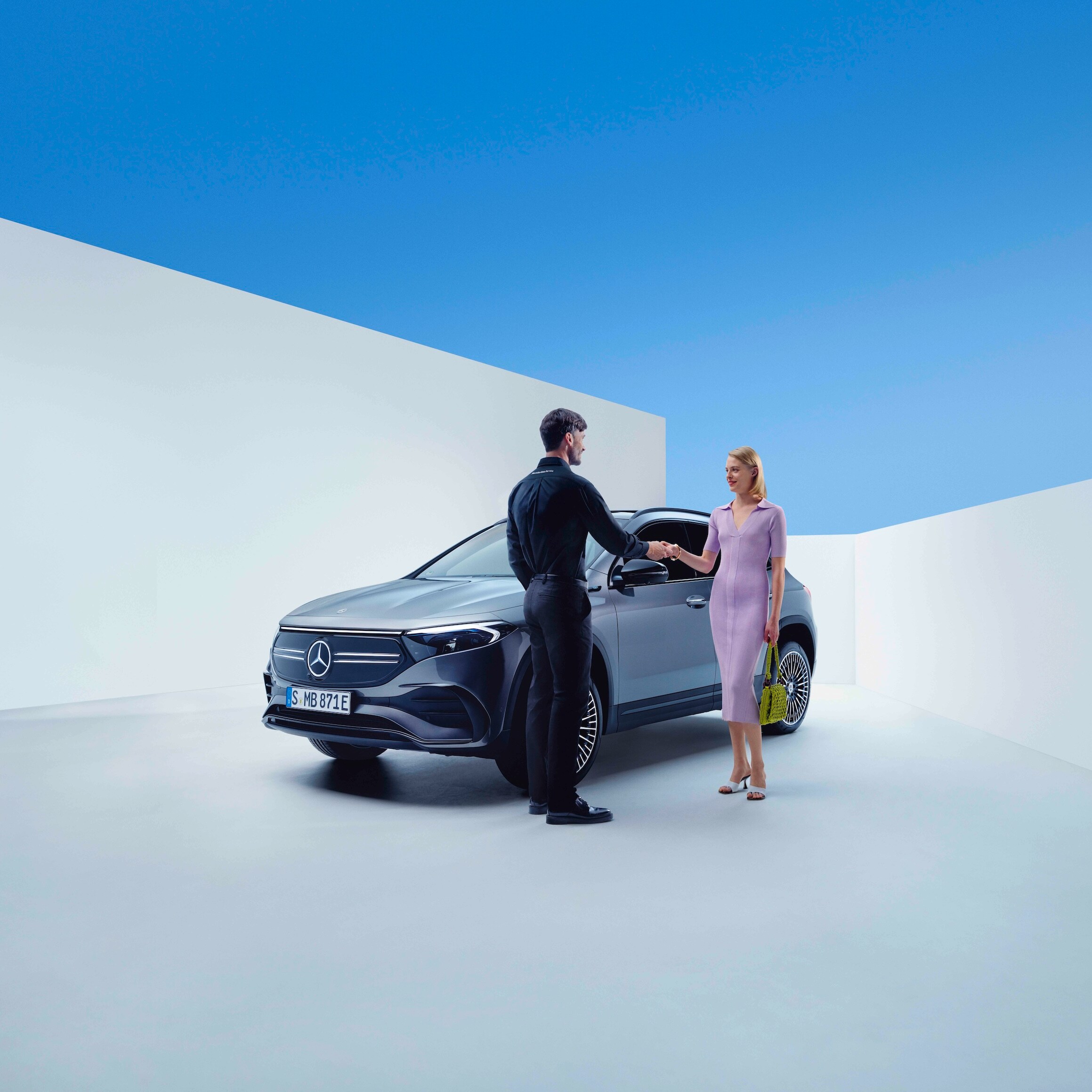 Un dipendente Mercedes-Benz e una donna si stringono la mano davanti a una Mercedes-Benz