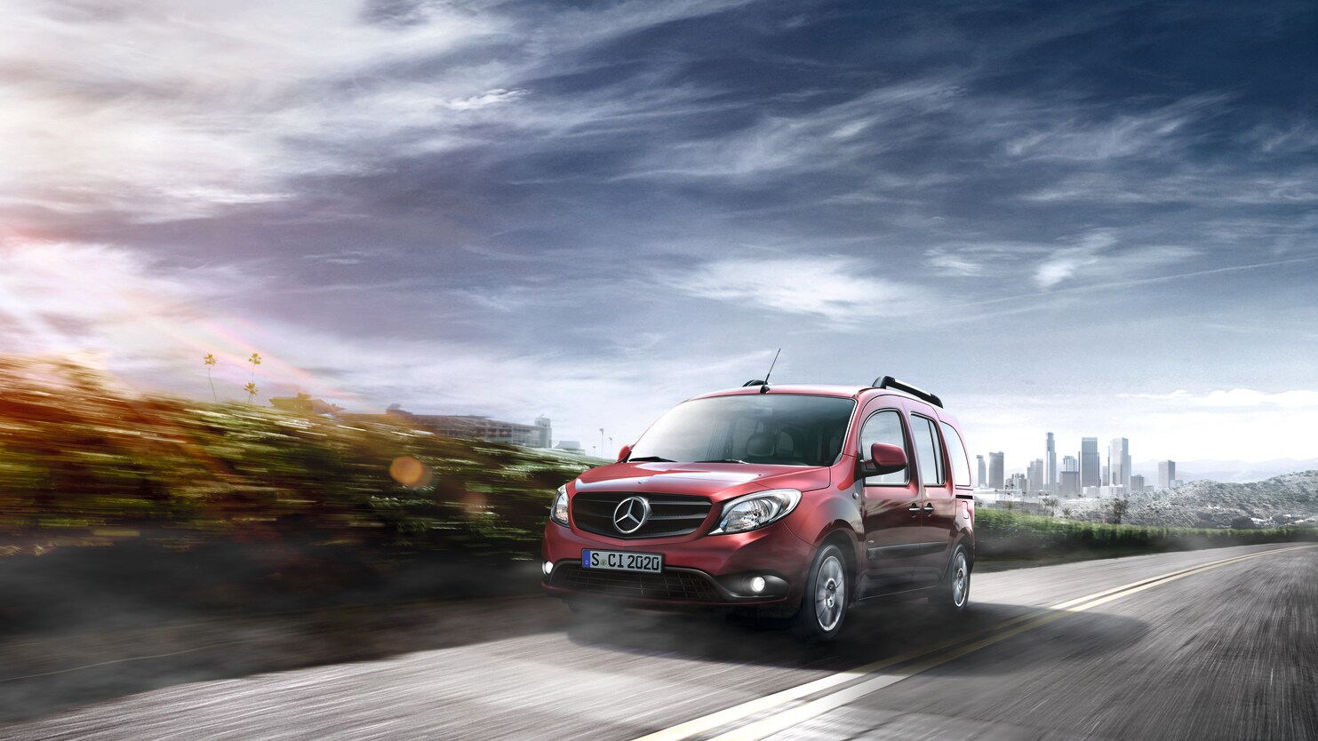 Un Mercedes-Benz Citan rosso mentre percorre una strada panoramica con lo skyline della città sullo sfondo