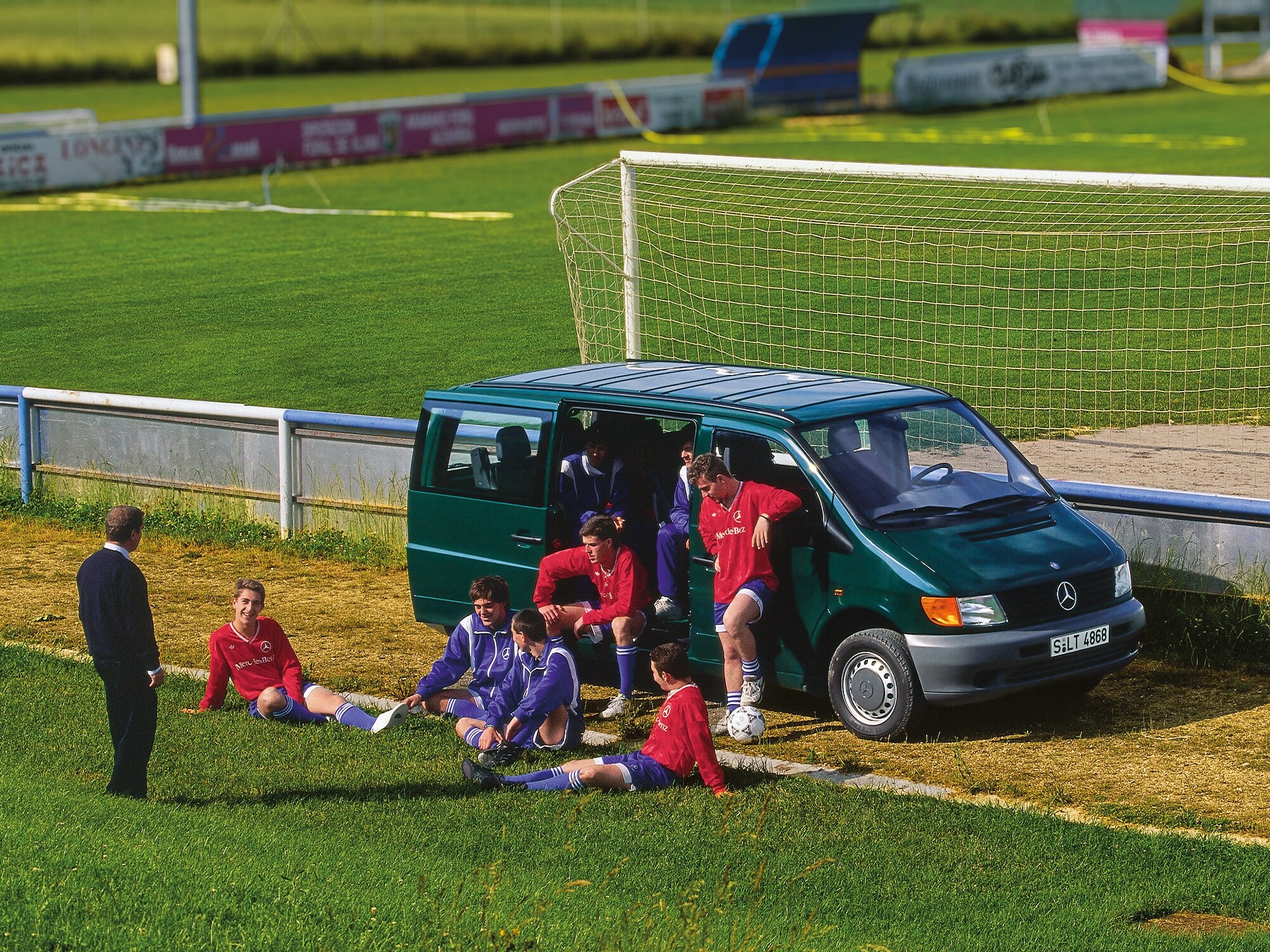 Un Vito di prima generazione parcheggiato accanto a un campo da calcio, con i giocatori della squadra nelle vicinanze