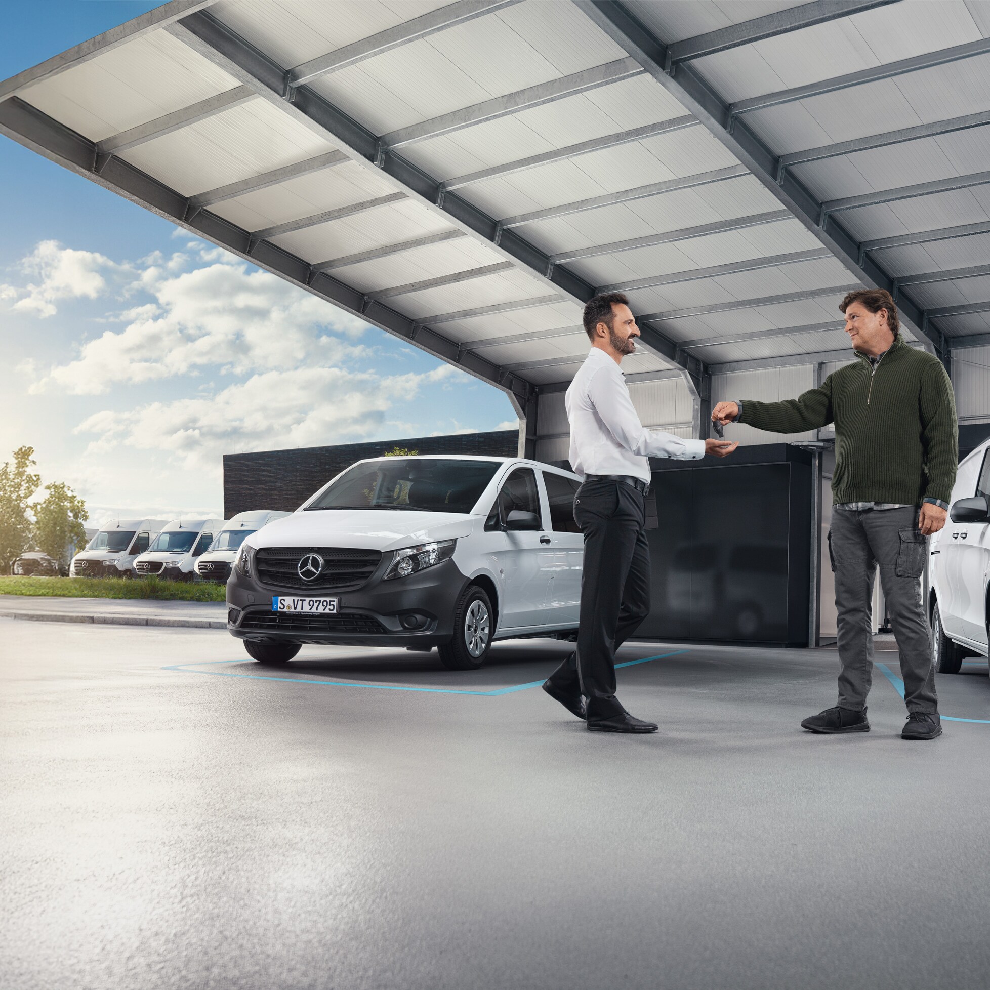 Due uomini discutono di fronte a una serie di furgoni Mercedes-Benz bianchi in una sala