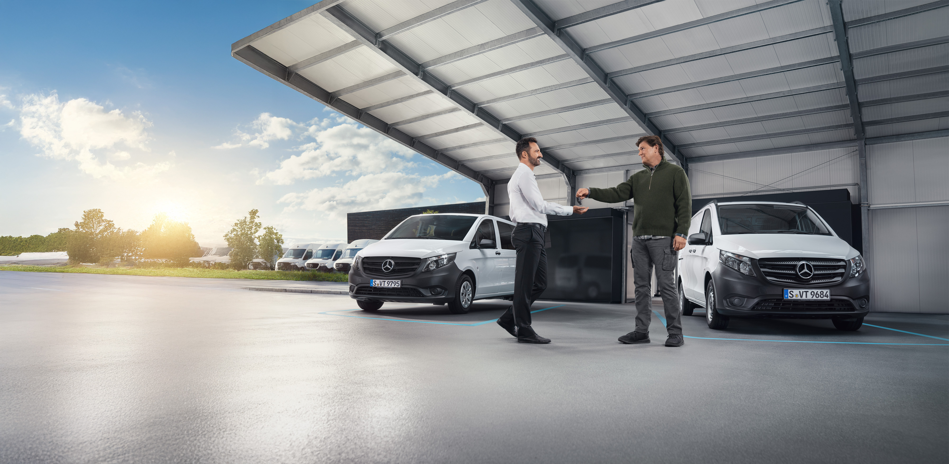 Mercedes-Benz | Van Care | Individual Support Due uomini discutono di fronte a una serie di furgoni Mercedes-Benz bianchi in una sala