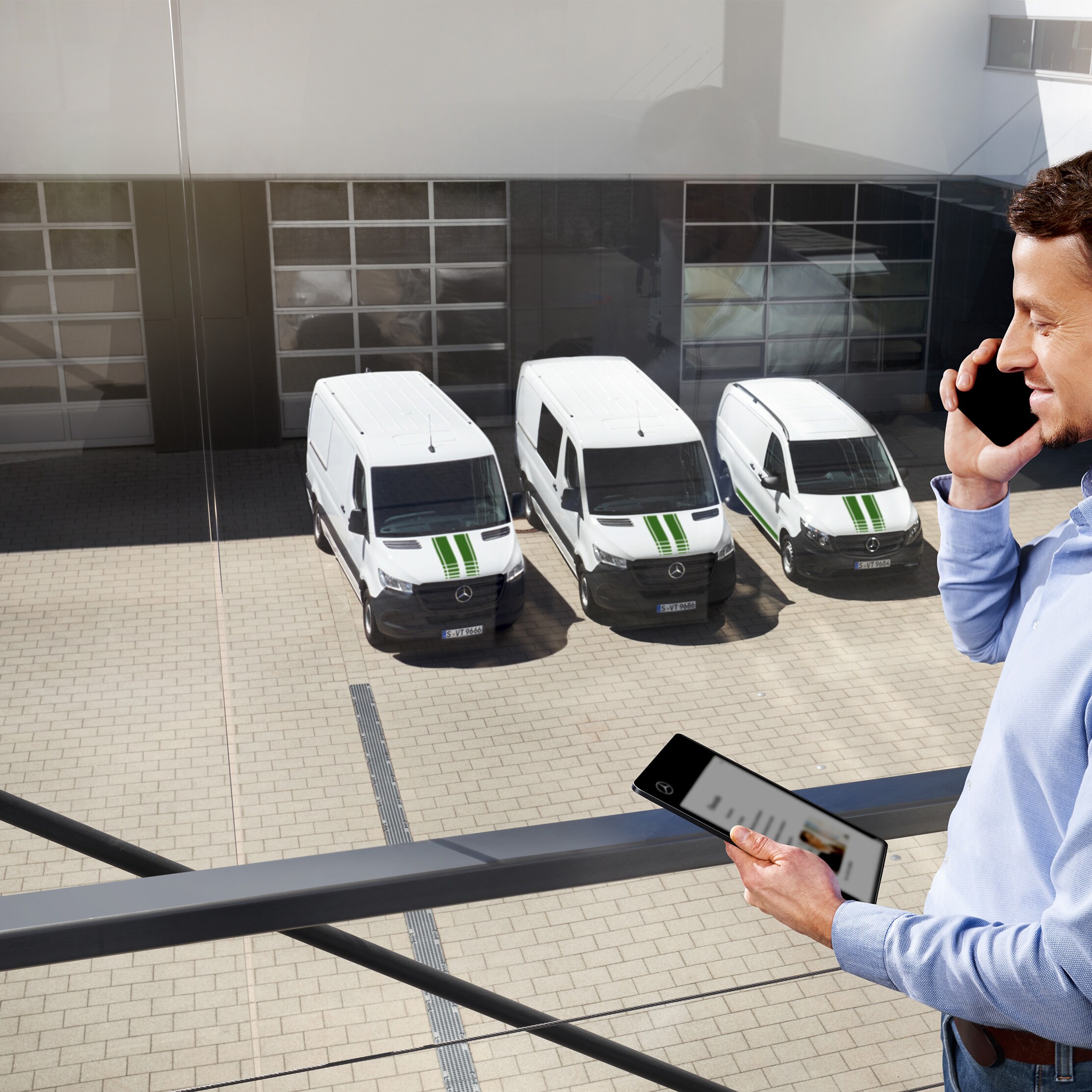 Cliente al telefono davanti a una flotta di furgoni Mercedes-Benz bianchi.