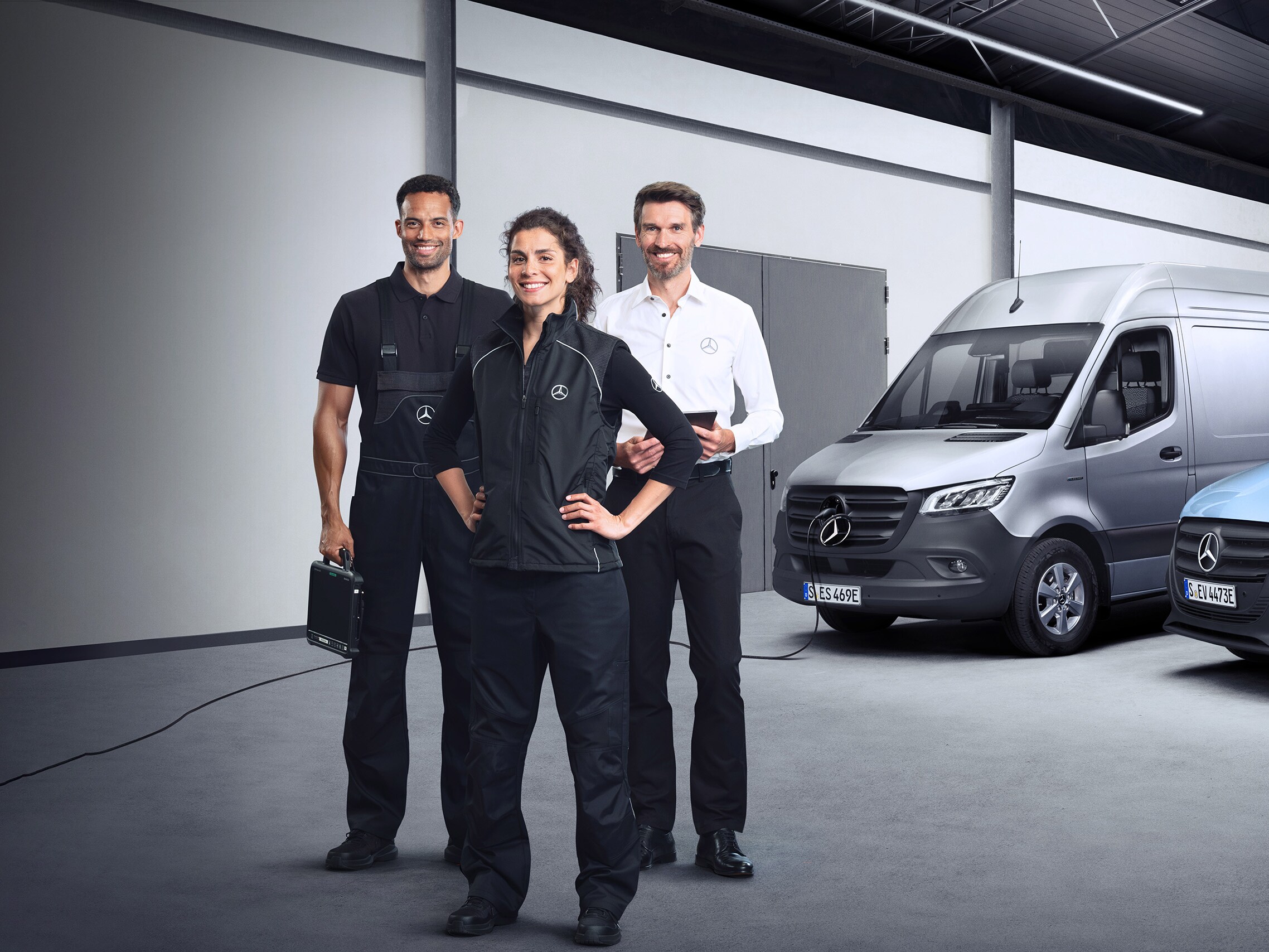 Tre addetti Mercedes-Benz Service davanti a veicoli commerciali elettrici Mercedes-Benz