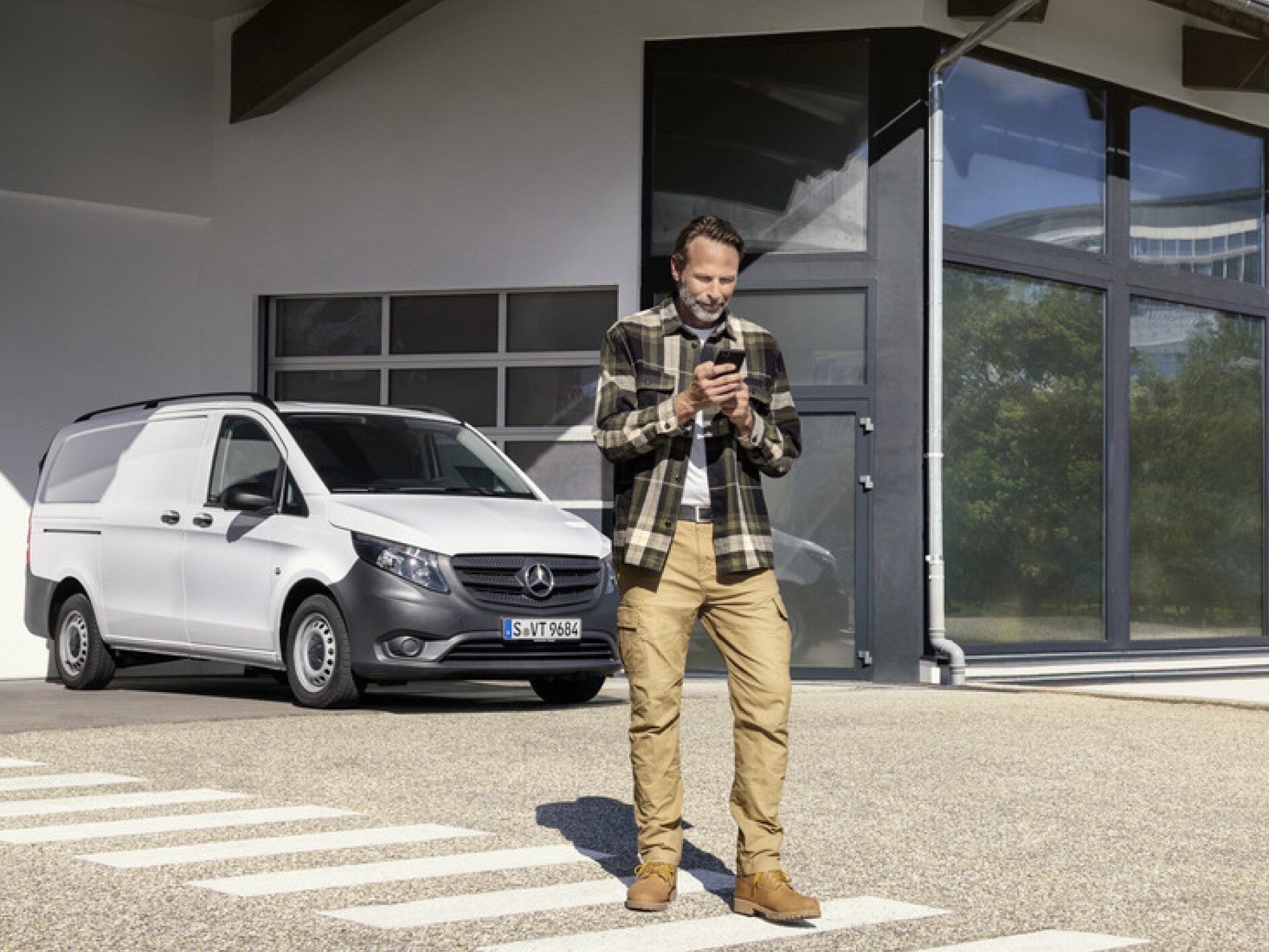 Una persona con uno smartphone davanti a un Mercedes-Benz Vito.