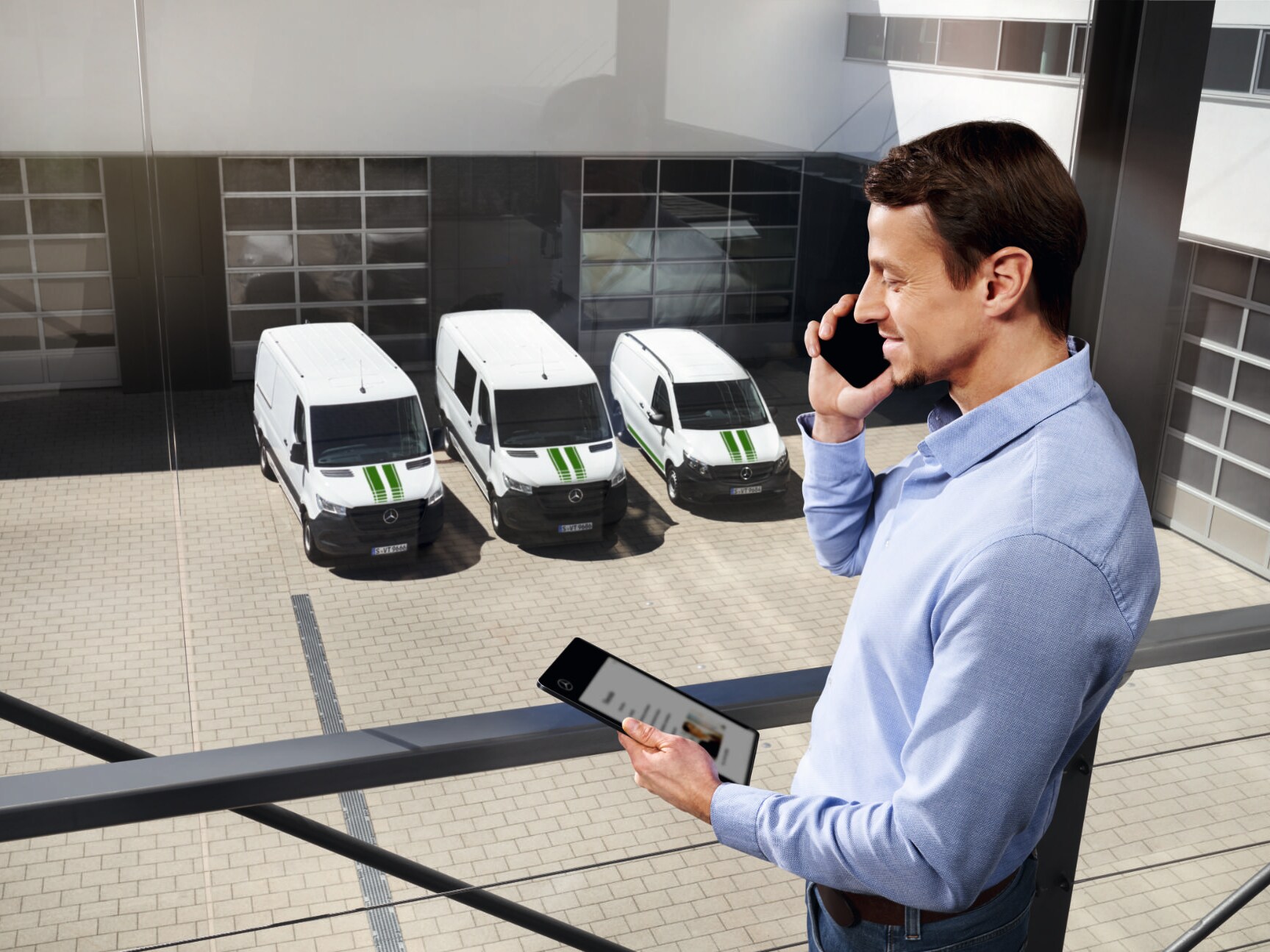 Un consulente Mercedes-Benz in piedi, con in mano un telefono e un tablet, e furgoni Mercedes-Benz sullo sfondo.