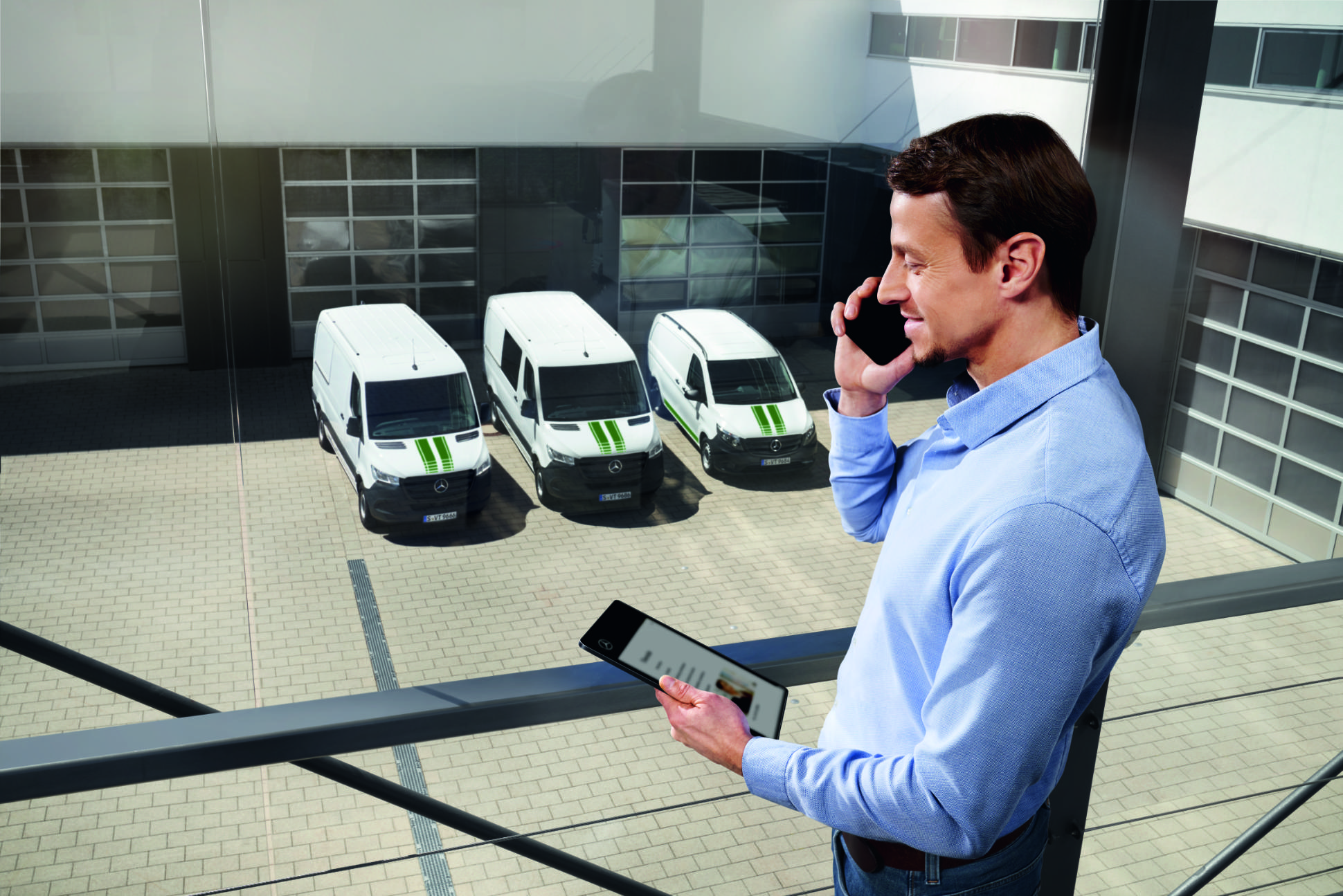 Van Uptime Monitor | Digital Extras | Mercedes-Benz Un consulente Mercedes-Benz in piedi, con in mano un telefono e un tablet, e furgoni Mercedes-Benz sullo sfondo.