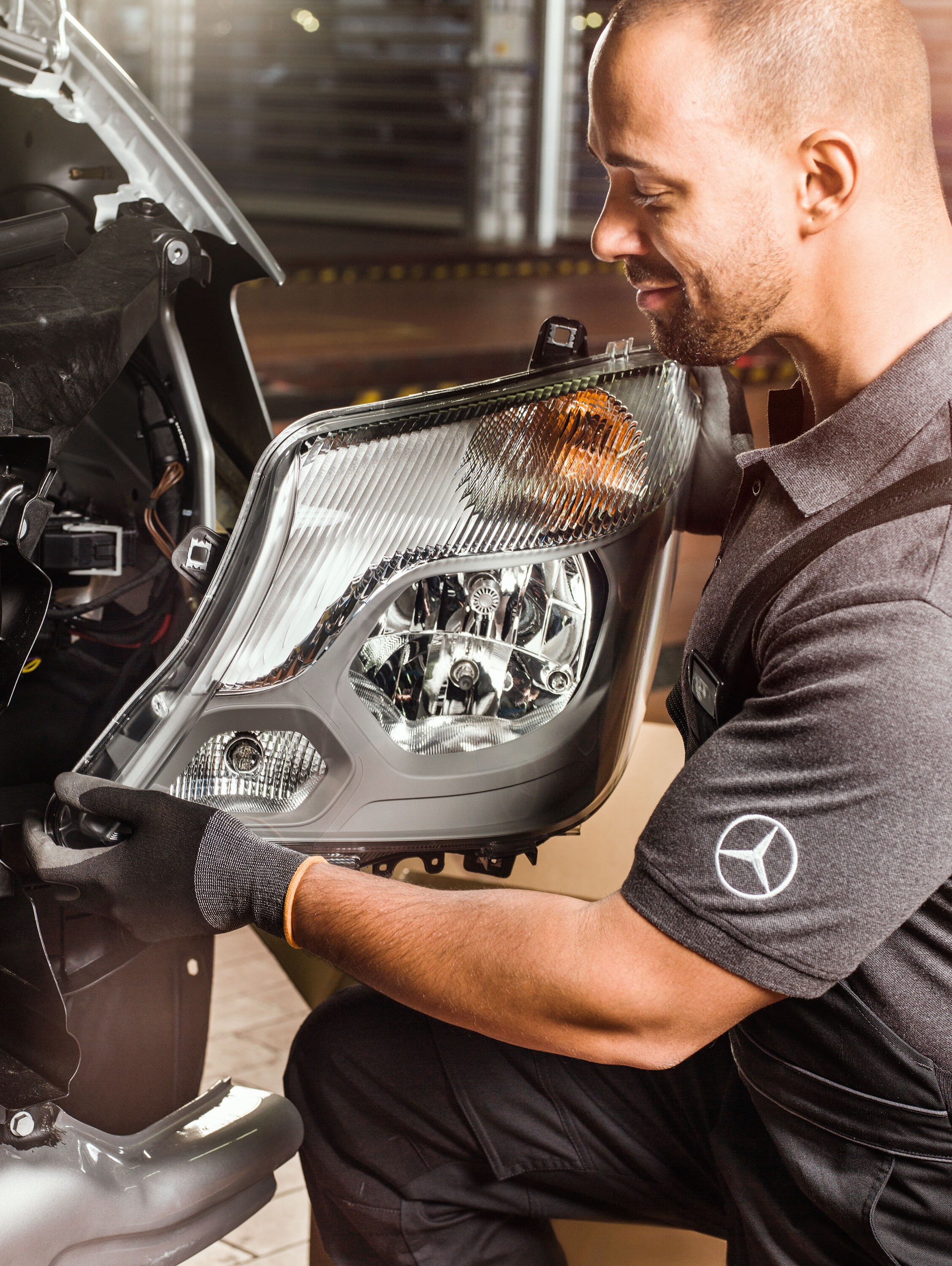 Un meccanico mentre controlla i componenti originali Mercedes-Benz davanti al motore di uno Sprinter aperto, confrontandoli con il catalogo ricambi Mercedes.