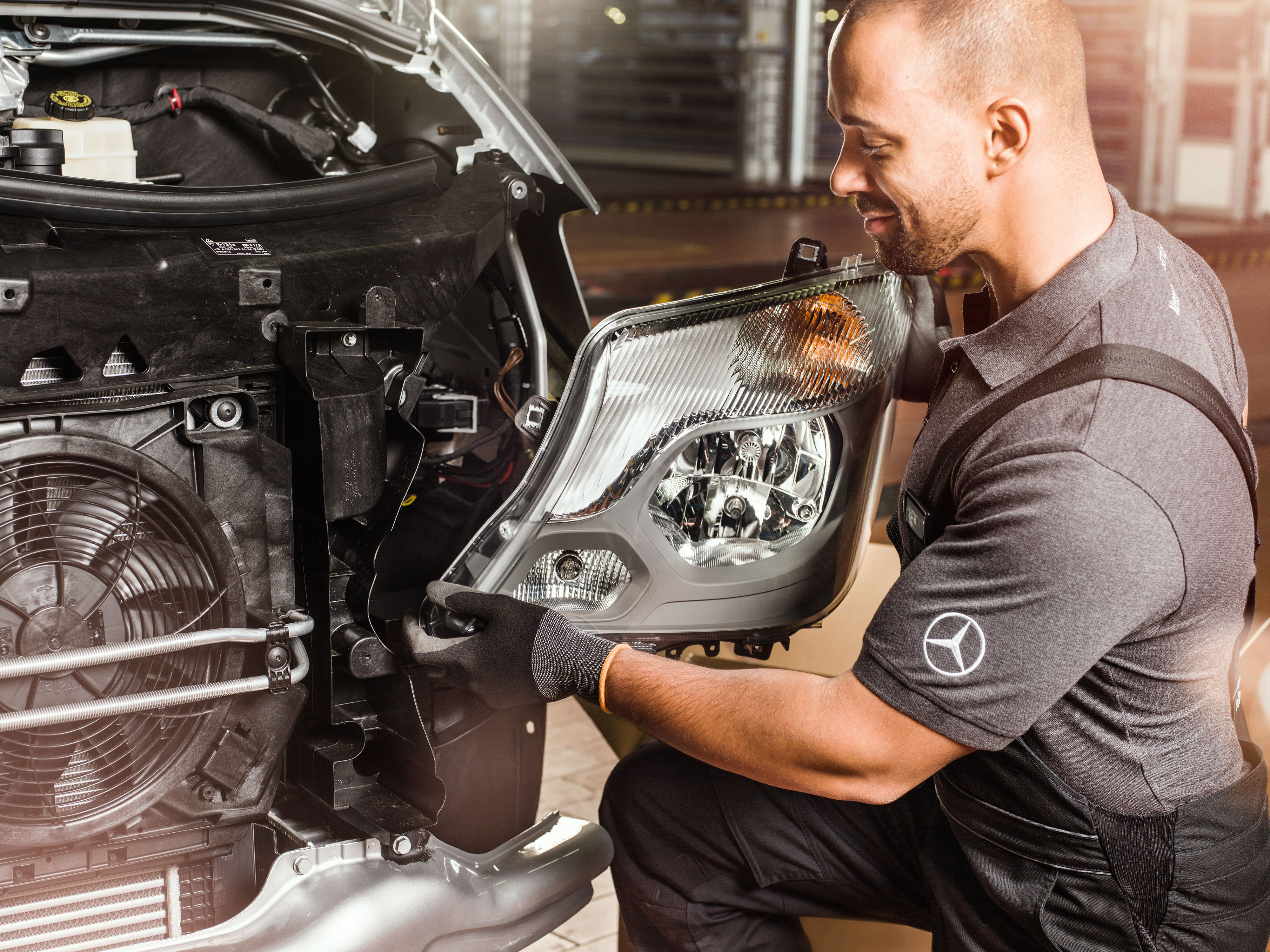Mercedes-Benz | Ricambi originali di qualità per i veicoli commerciali Un meccanico mentre controlla i componenti originali Mercedes-Benz davanti al motore di uno Sprinter aperto, confrontandoli con il catalogo ricambi Mercedes.