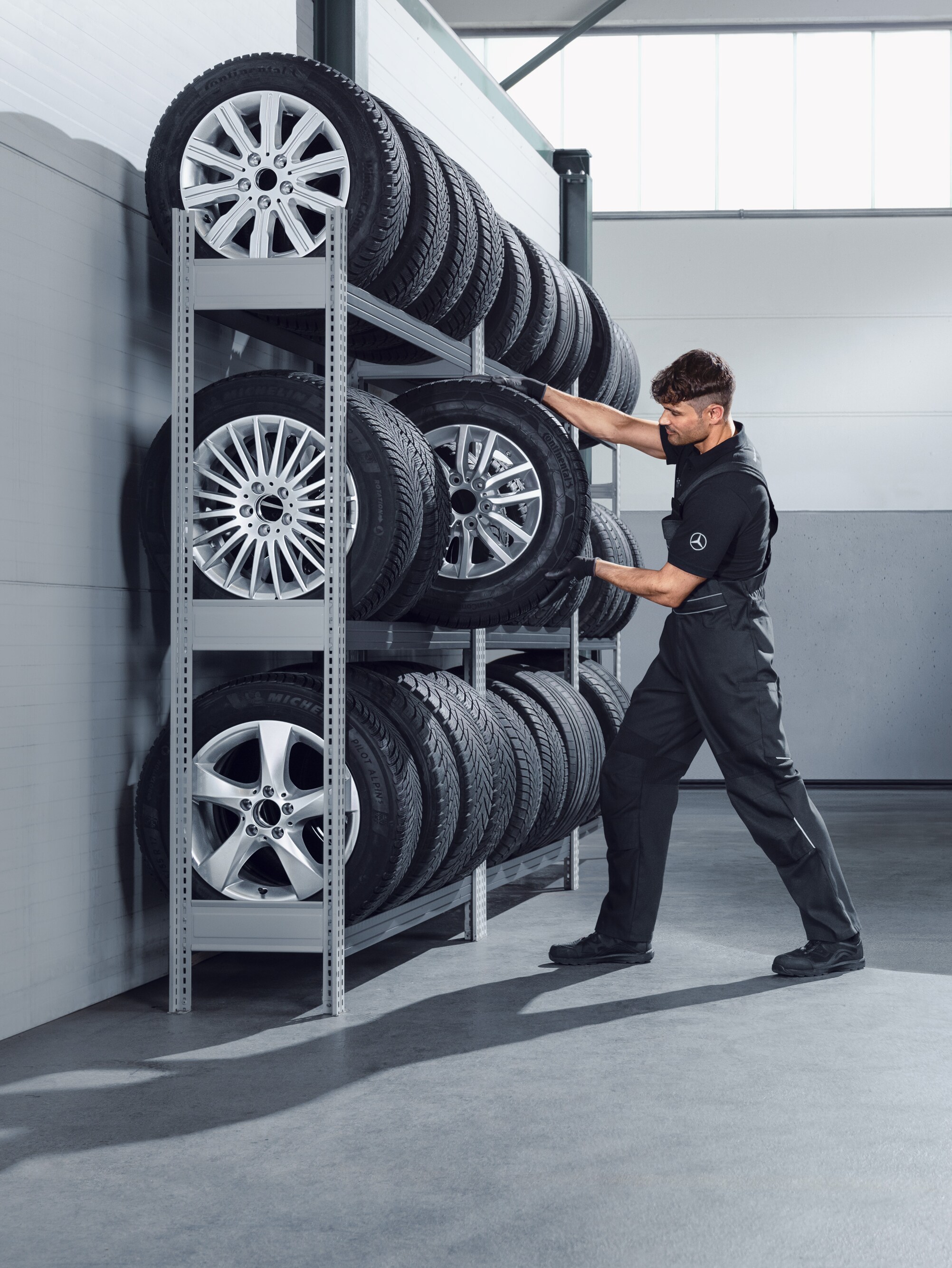 Un meccanico sceglie dallo scaffale dell'officina le ruote invernali complete Mercedes-Benz per uno Sprinter bianco.