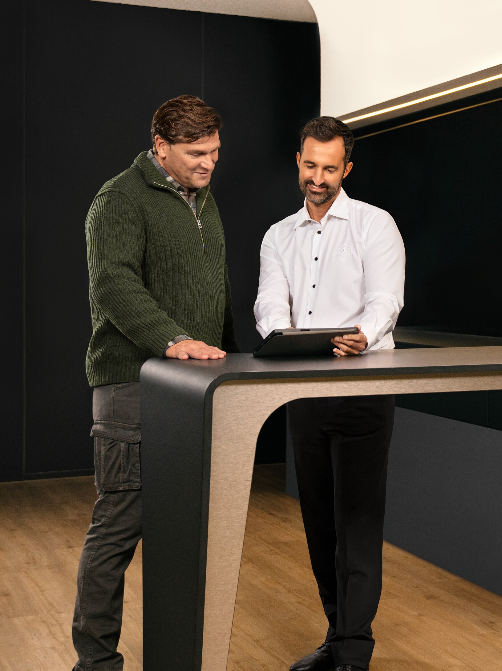 Due uomini si consultano in piedi intorno a un tavolo mentre guardano un iPad.