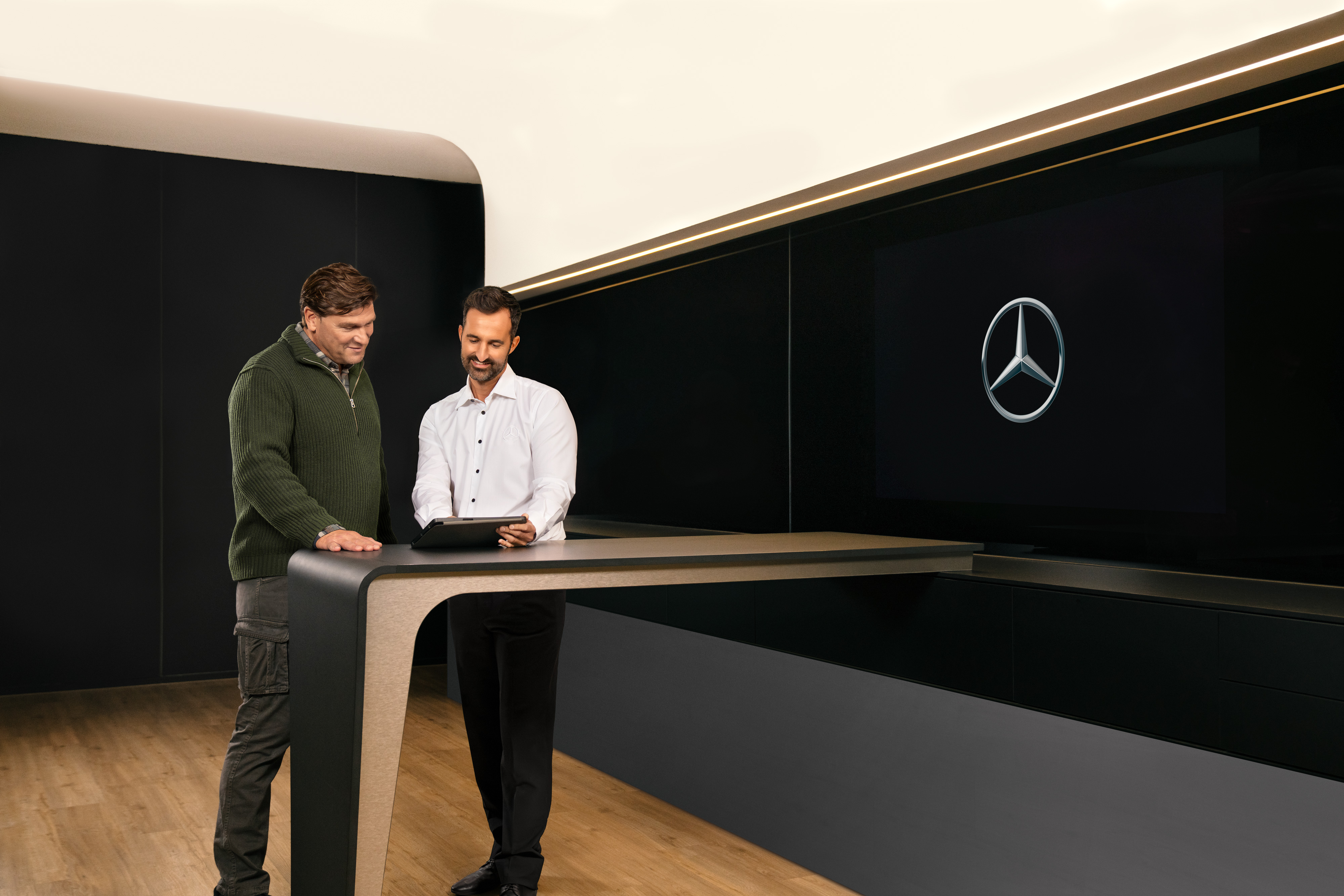 Mercedes-Benz | ServiceCare per i veicoli commerciali Due uomini si consultano in piedi intorno a un tavolo mentre guardano un iPad.