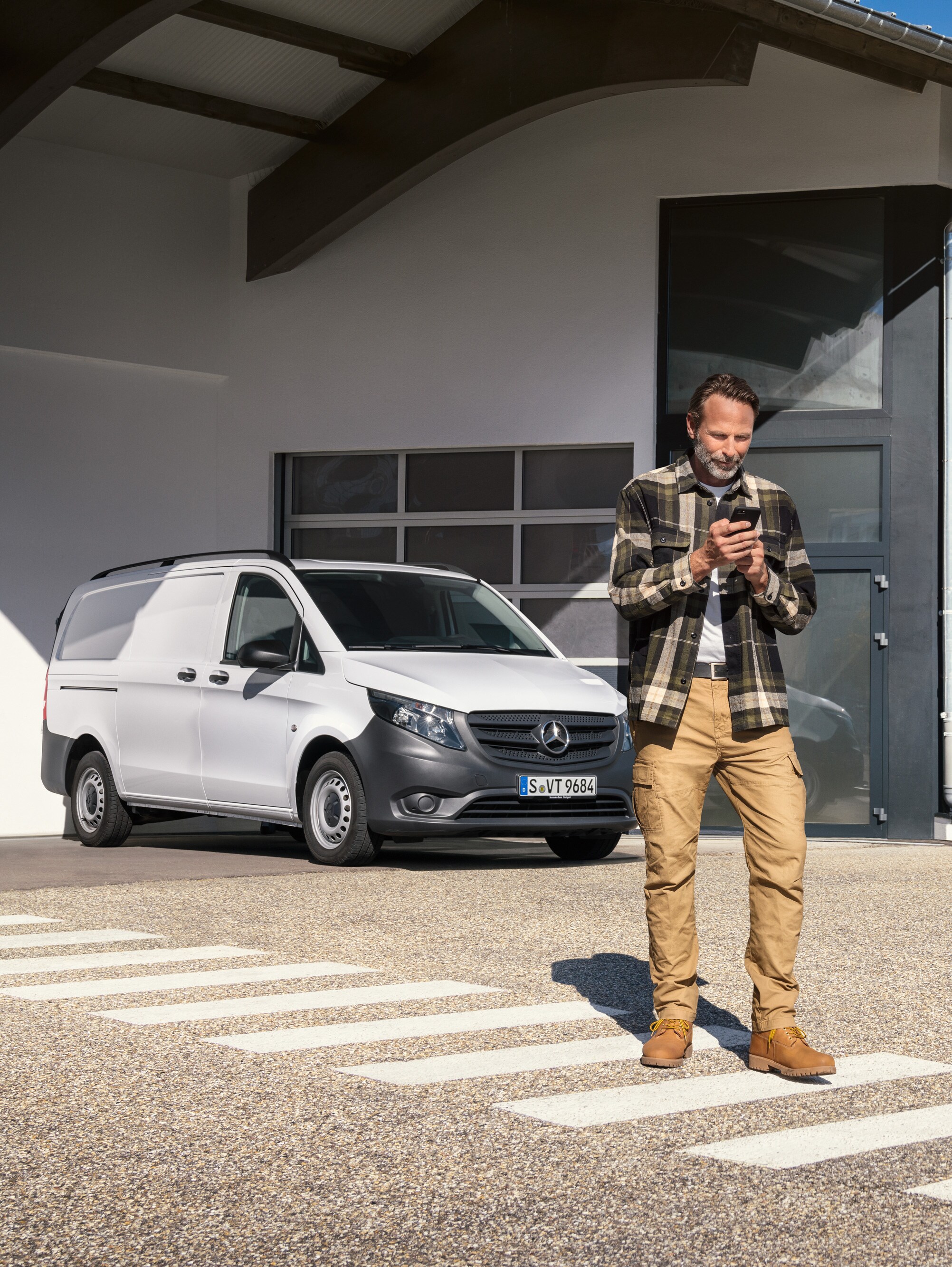 Un uomo in piedi davanti a un veicolo commerciale Mercedes-Benz Vito bianco mentre utilizza il suo smartphone.