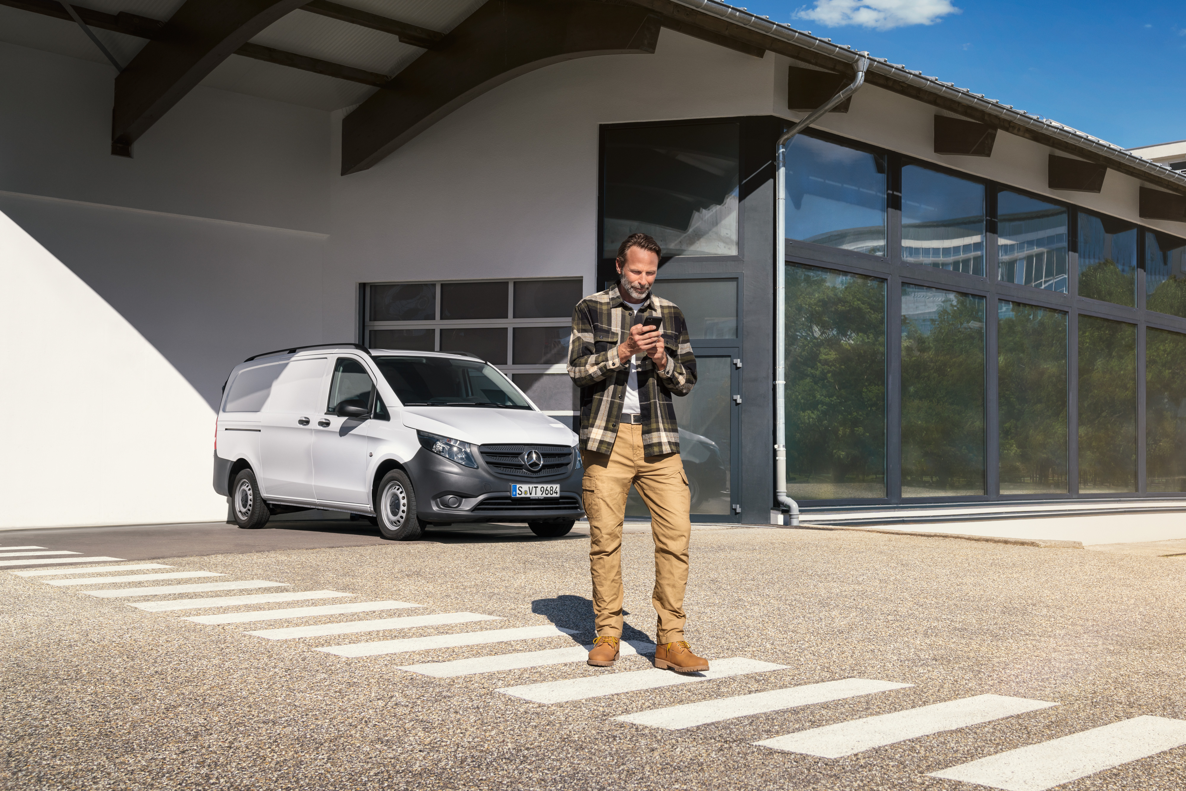 Mercedes-Benz | Servizio assistenza veicoli elettrici | Assistenza digitale Un uomo in piedi davanti a un veicolo commerciale Mercedes-Benz Vito bianco mentre utilizza il suo smartphone.