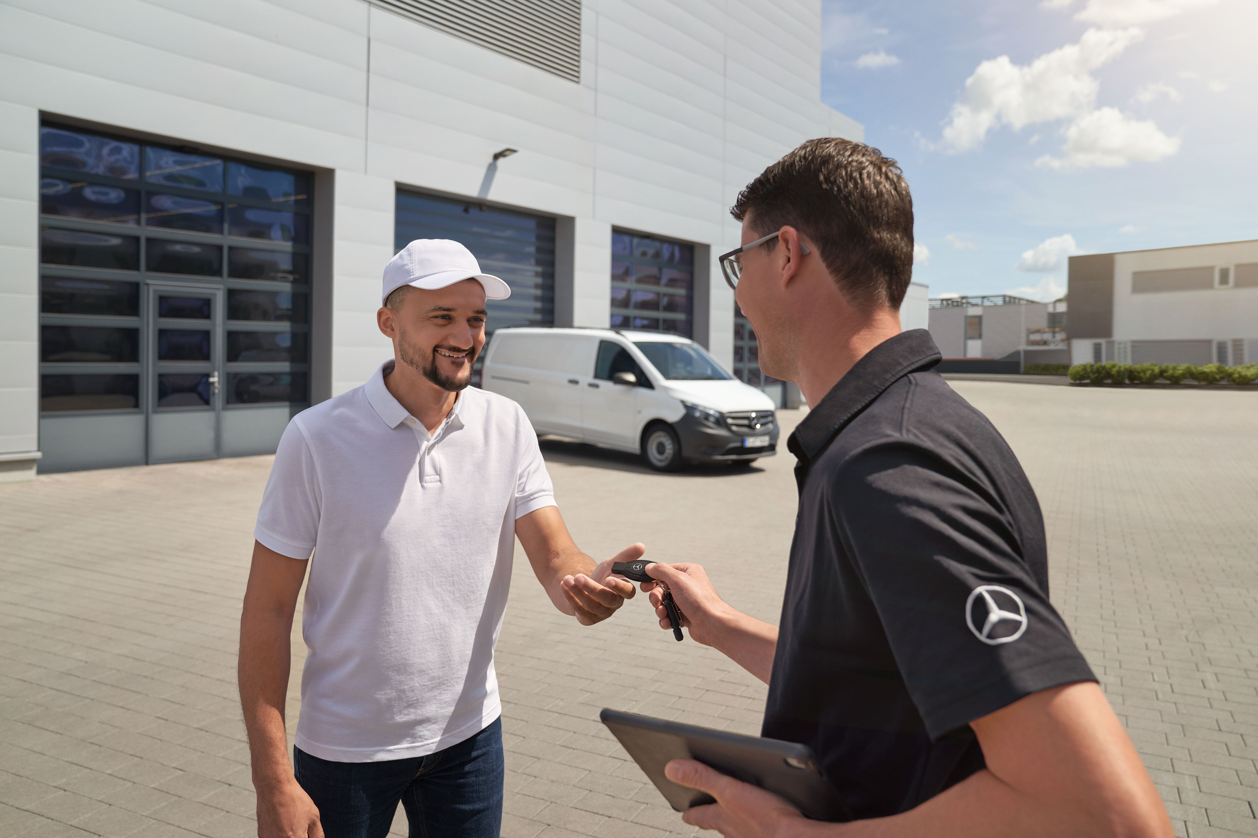 Mercedes-Benz | Manutenzione | Ritiro e consegna Un rappresentante del servizio assistenza Mercedes-Benz consegna le chiavi a un cliente con un veicolo commerciale Mercedes-Benz Vito bianco sullo sfondo.