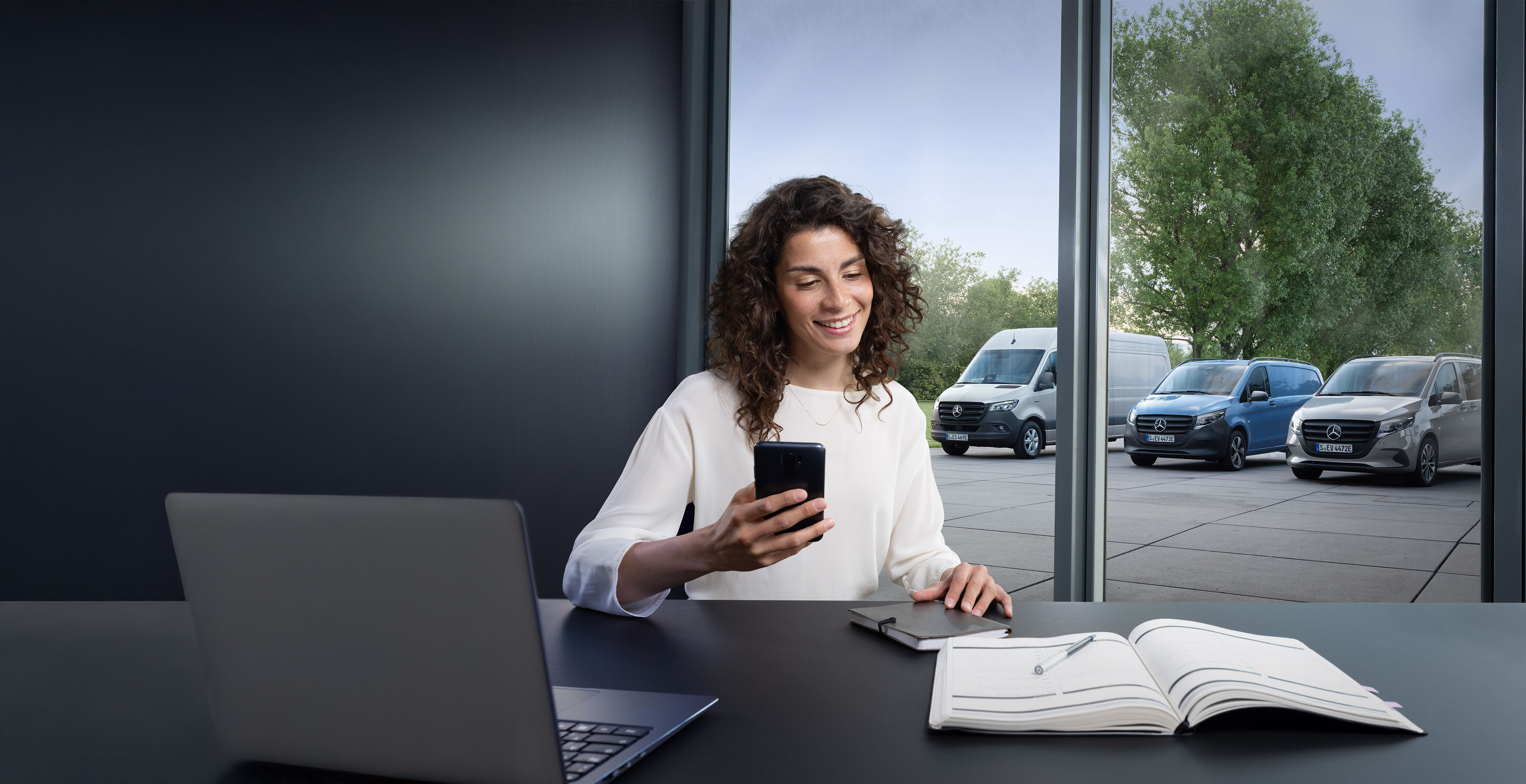 Mercedes-Benz | Repair | Service partner search Cliente al telefono davanti a una serie di furgoni Mercedes-Benz.