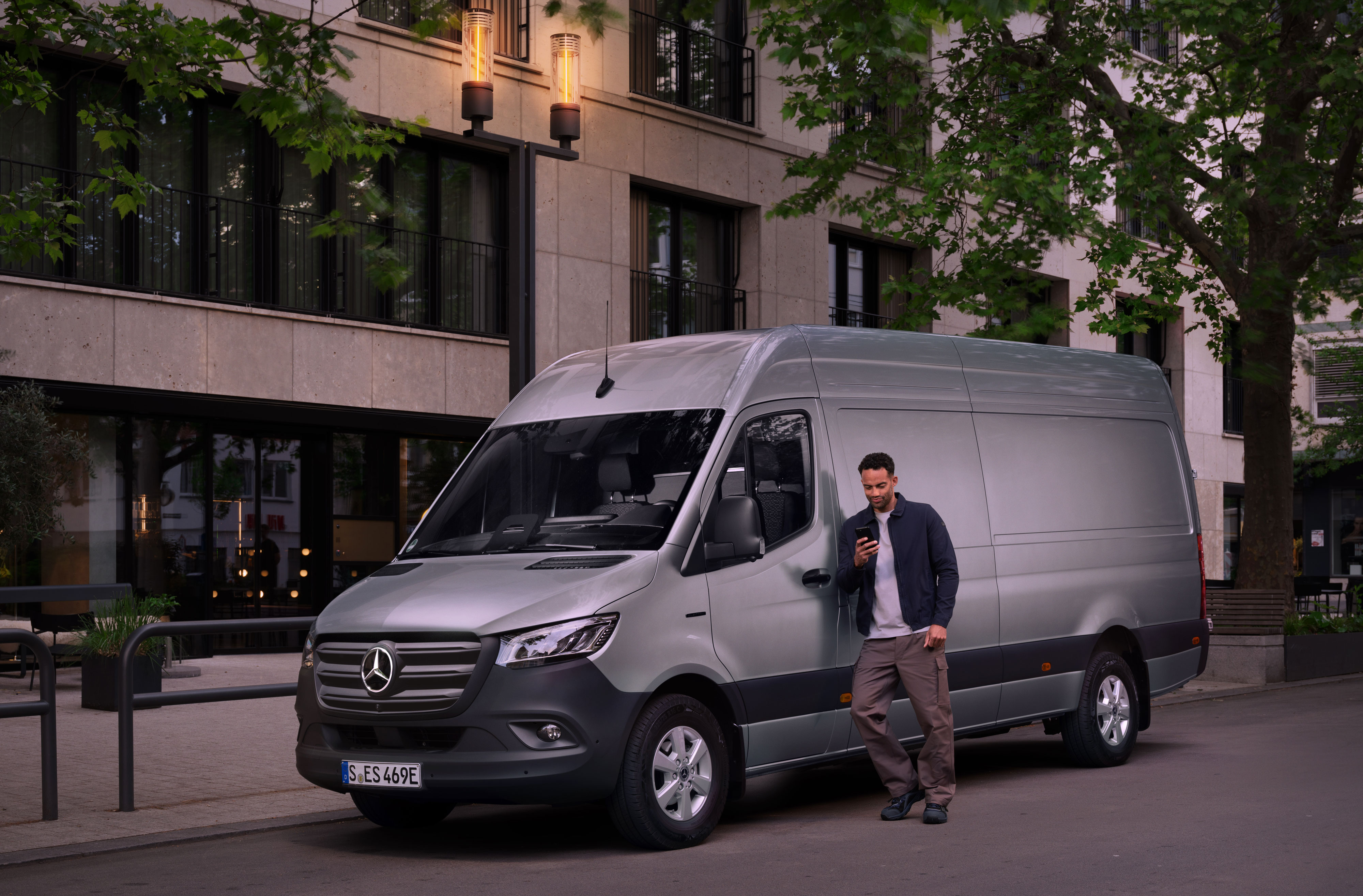 Mercedes-Benz | Riparazione | Rapporto sul danno digitale Un uomo appoggiato a un Mercedes-Benz Sprinter color argento mentre sta compilando un rapporto sui danni con il suo cellulare.