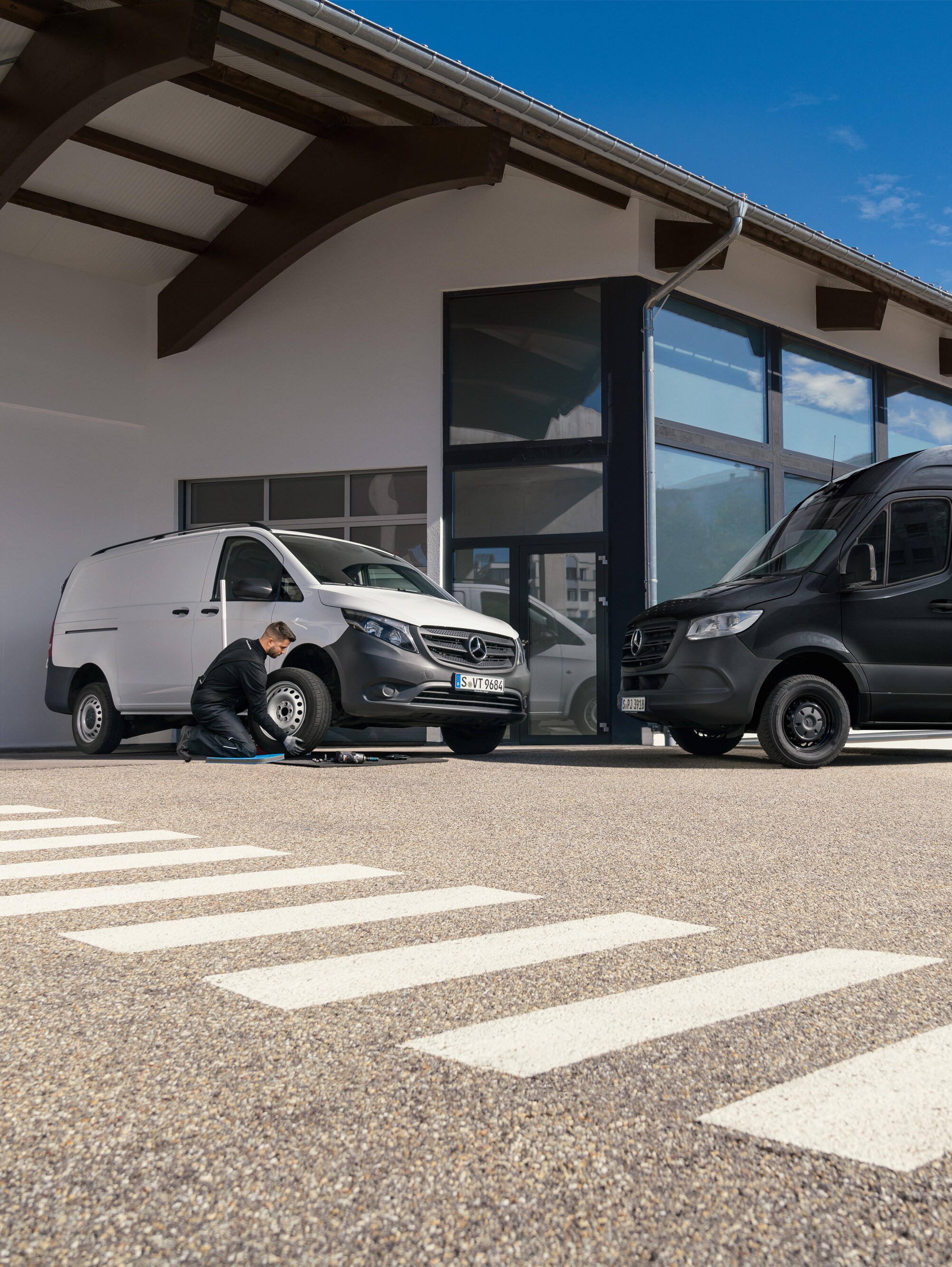 Un tecnico cambia uno pneumatico a un veicolo commerciale Mercedes-Benz Vito bianco davanti a uno showroom.