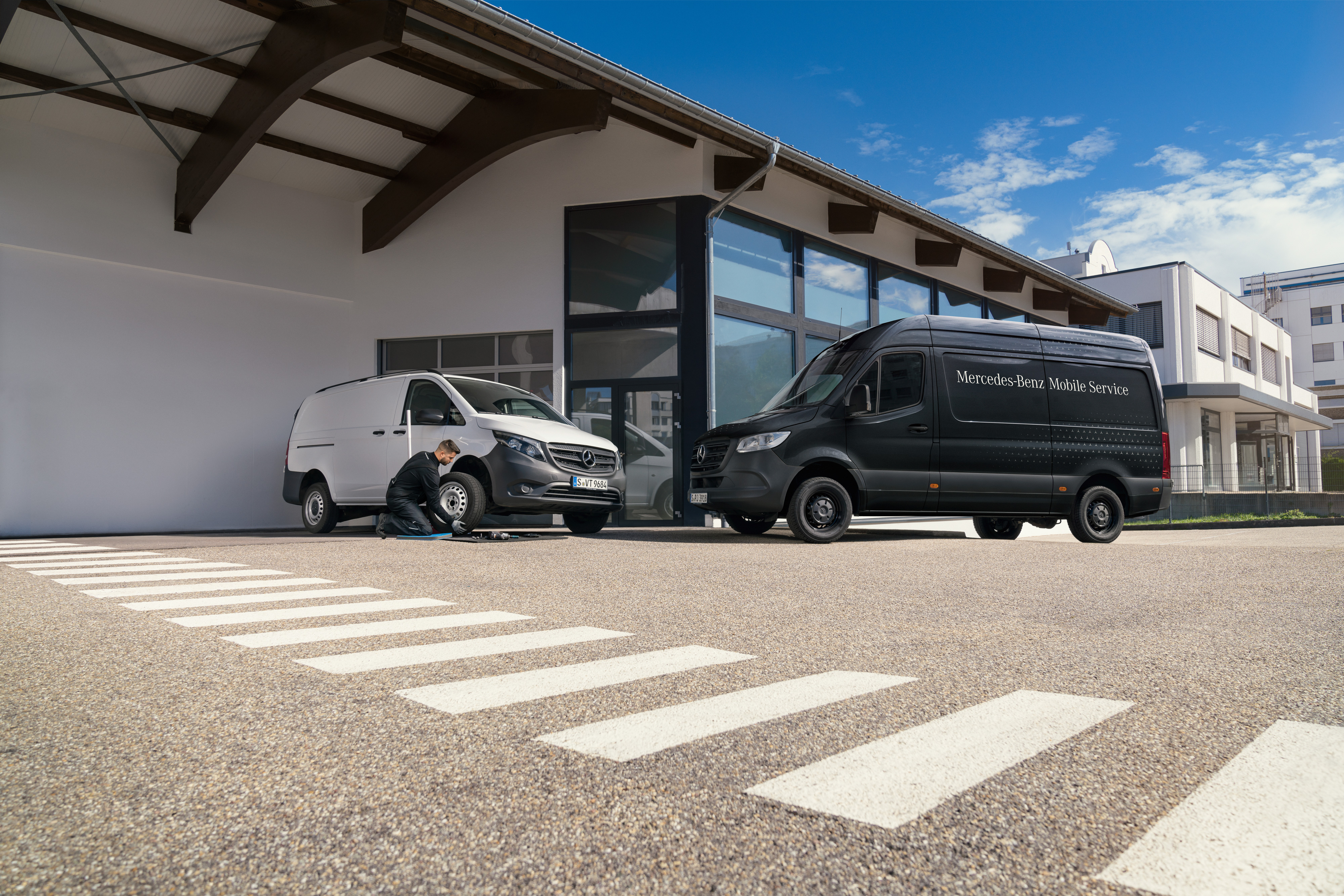 Mercedes-Benz | Mobile Service | Impianto frenante Un tecnico cambia uno pneumatico a un veicolo commerciale Mercedes-Benz Vito bianco davanti a uno showroom.