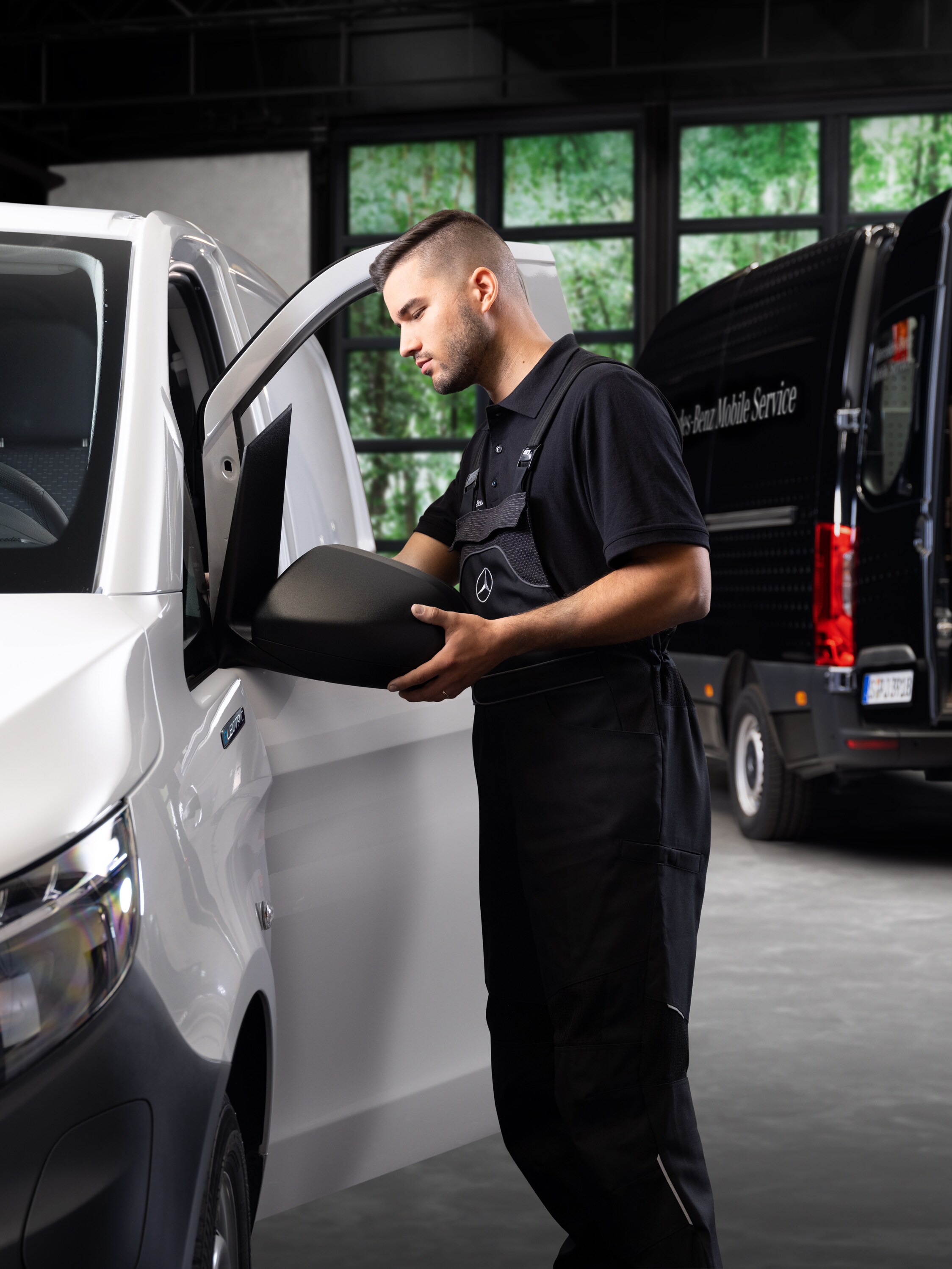 Un tecnico sostituisce un retrovisore esterno su un veicolo commerciale Mercedes-Benz Vito bianco.