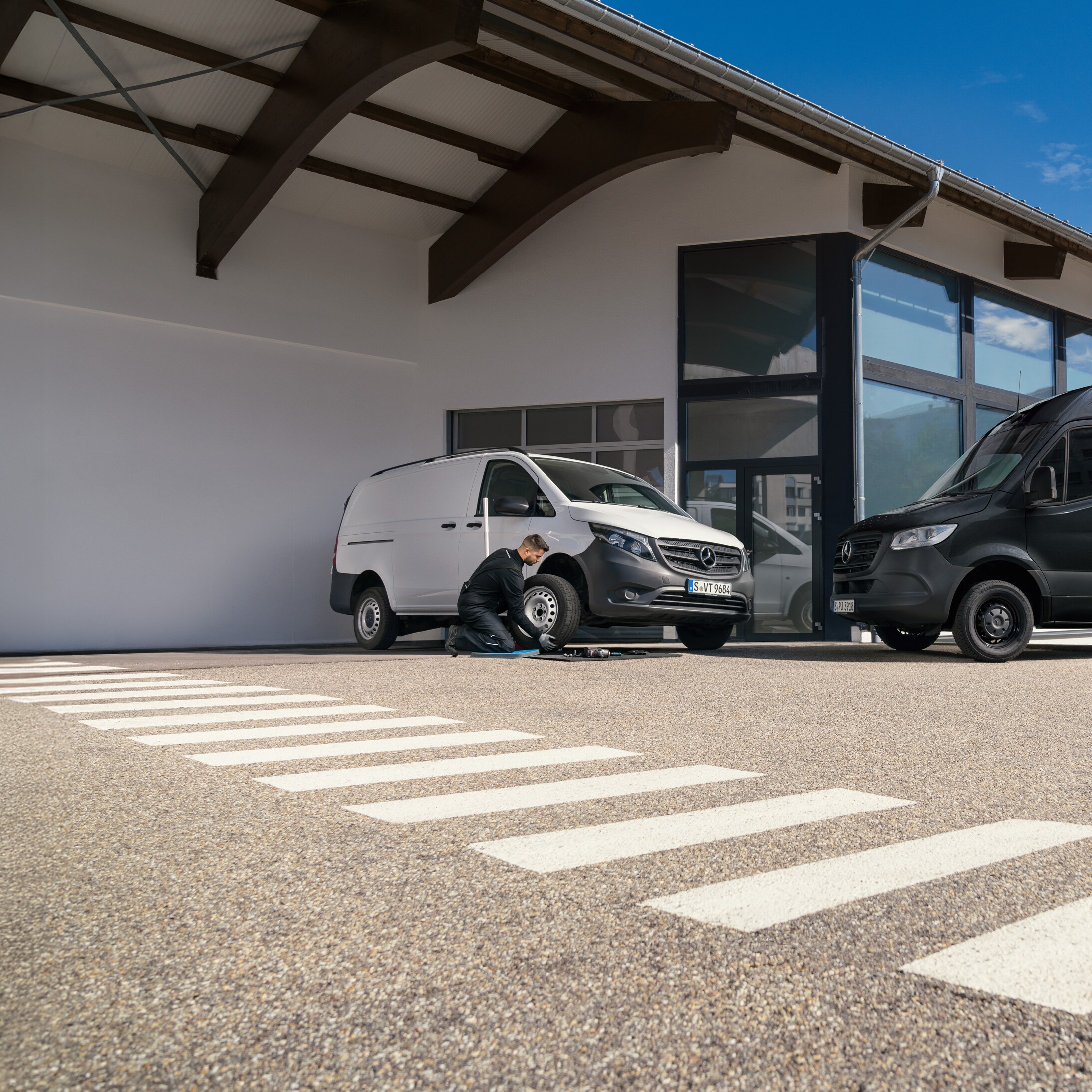 Un tecnico sostituisce uno pneumatico su un furgone Mercedes-Benz Vito bianco in un parcheggio.