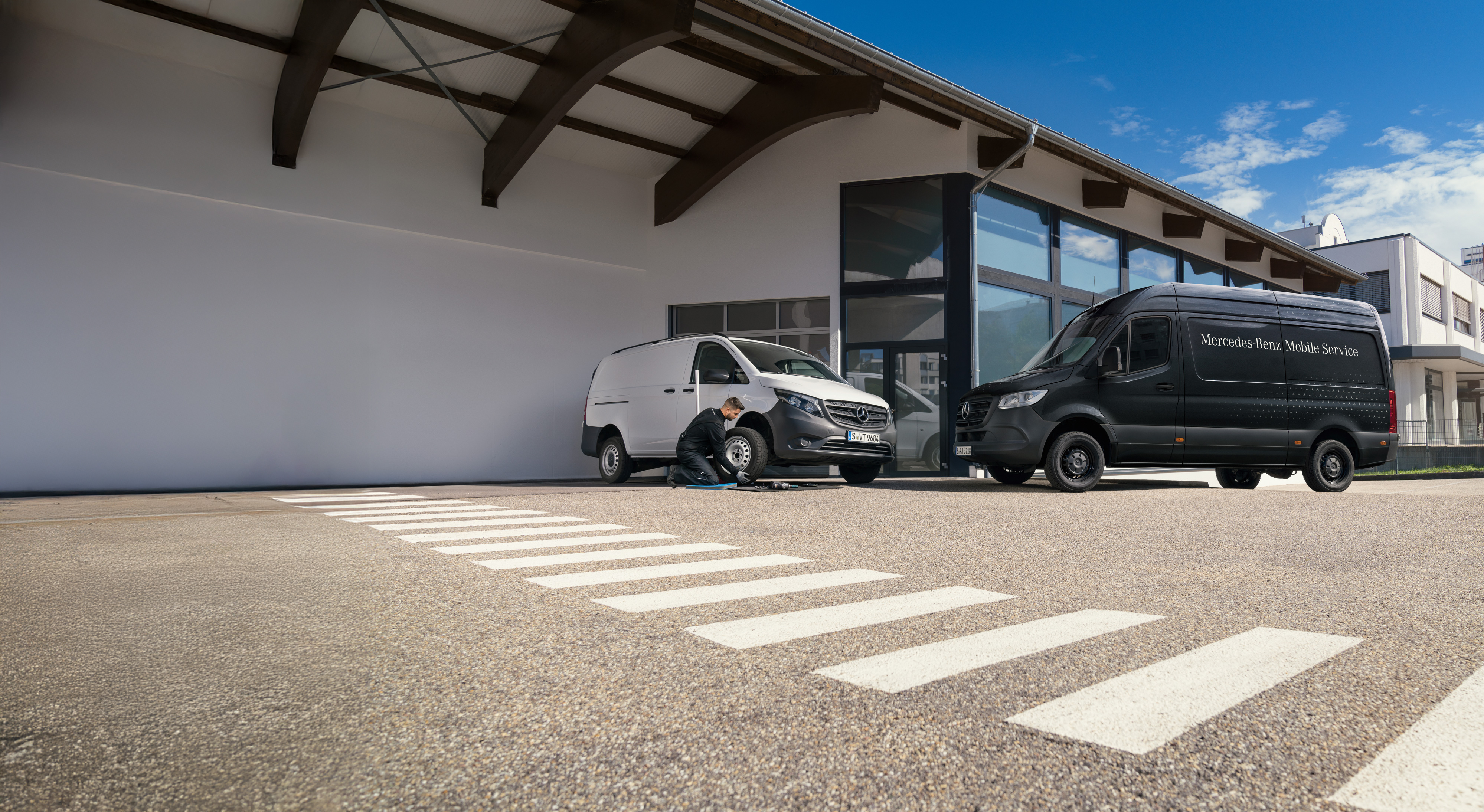 Mercedes-Benz | Mobile Service | Request a service Un tecnico sostituisce uno pneumatico su un furgone Mercedes-Benz Vito bianco in un parcheggio.