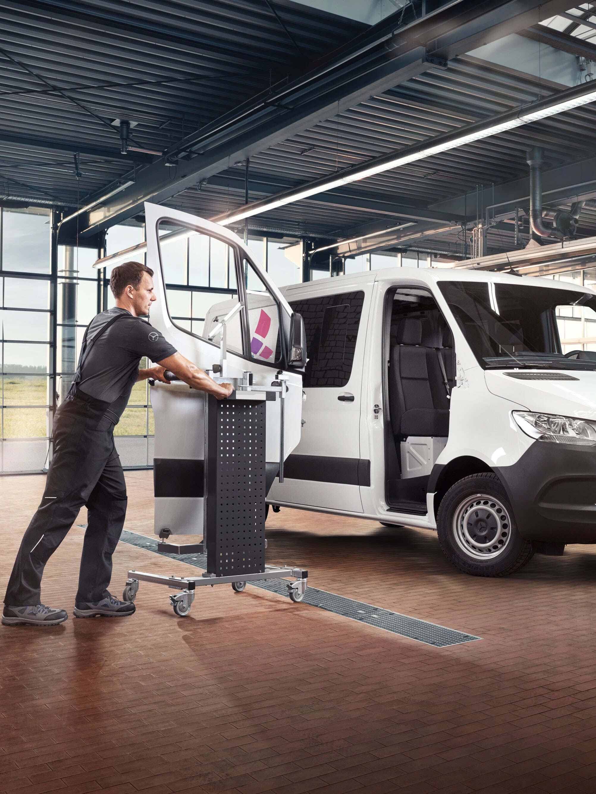 Un meccanico mentre monta la porta di un Mercedes-Benz Sprinter bianco.