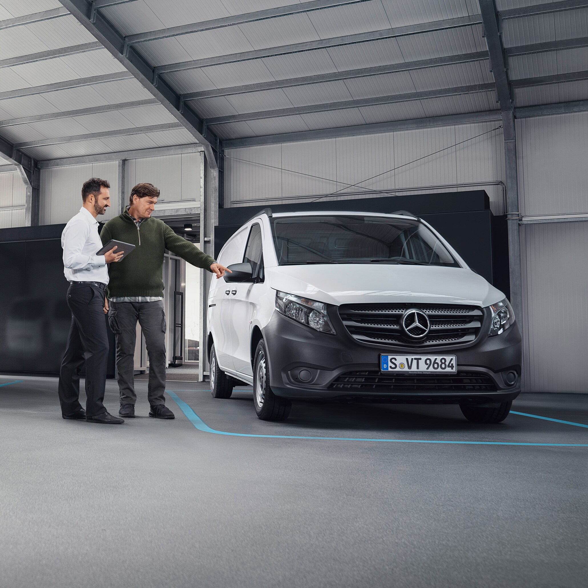 Un operatore del servizio assistenza clienti Mercedes-Benz con un cliente nella sede di un Mercedes-Benz Service davanti a un veicolo commerciale.