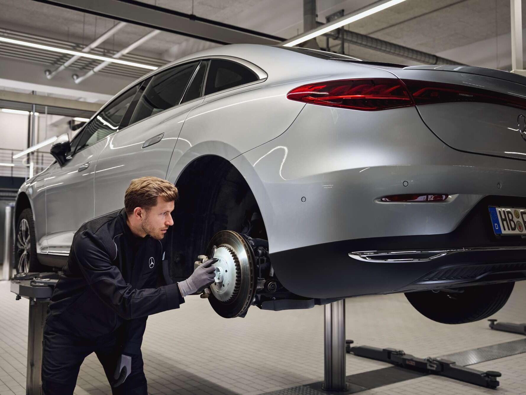 Un veicolo Mercedes-Benz sollevato su un ponte mentre un tecnico ispeziona l'impianto frenante posteriore per la sostituzione dei componenti originali.