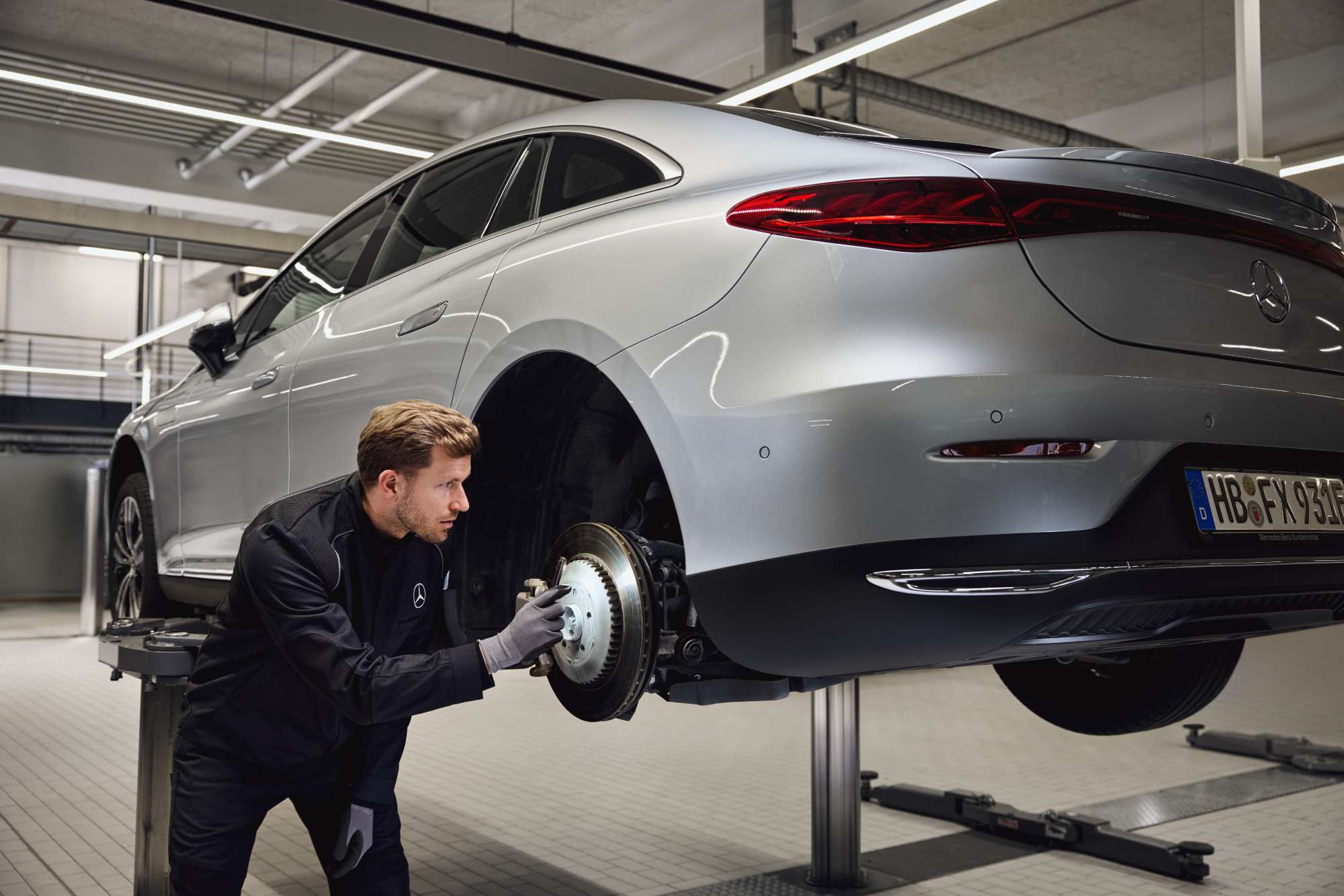 Sostituzione dei freni originali Mercedes-Benz Un veicolo Mercedes-Benz sollevato su un ponte mentre un tecnico ispeziona l'impianto frenante posteriore per la sostituzione dei componenti originali.
