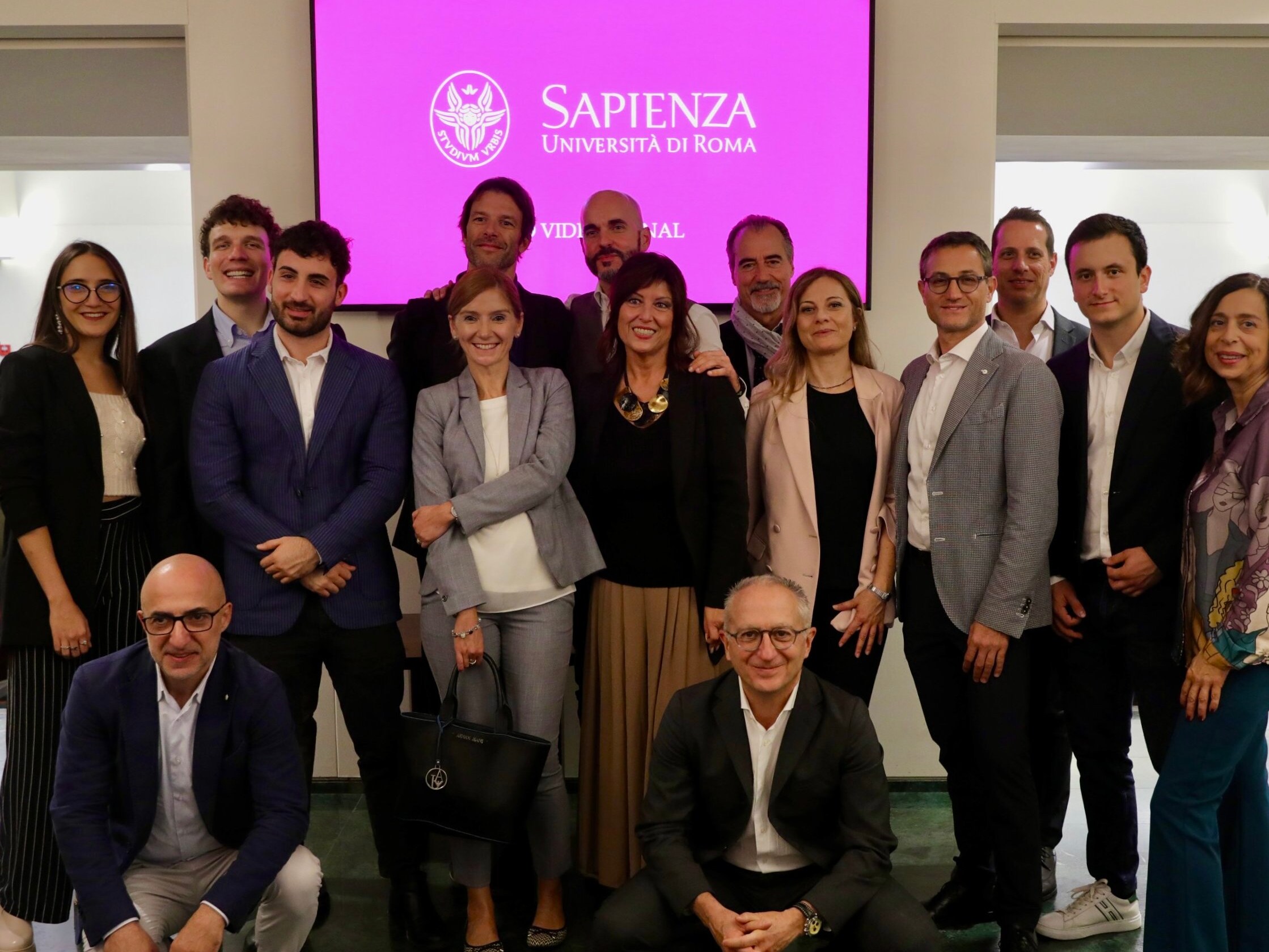 Foto di gruppo con sullo sfondo il logo dell'Università La Sapienza.