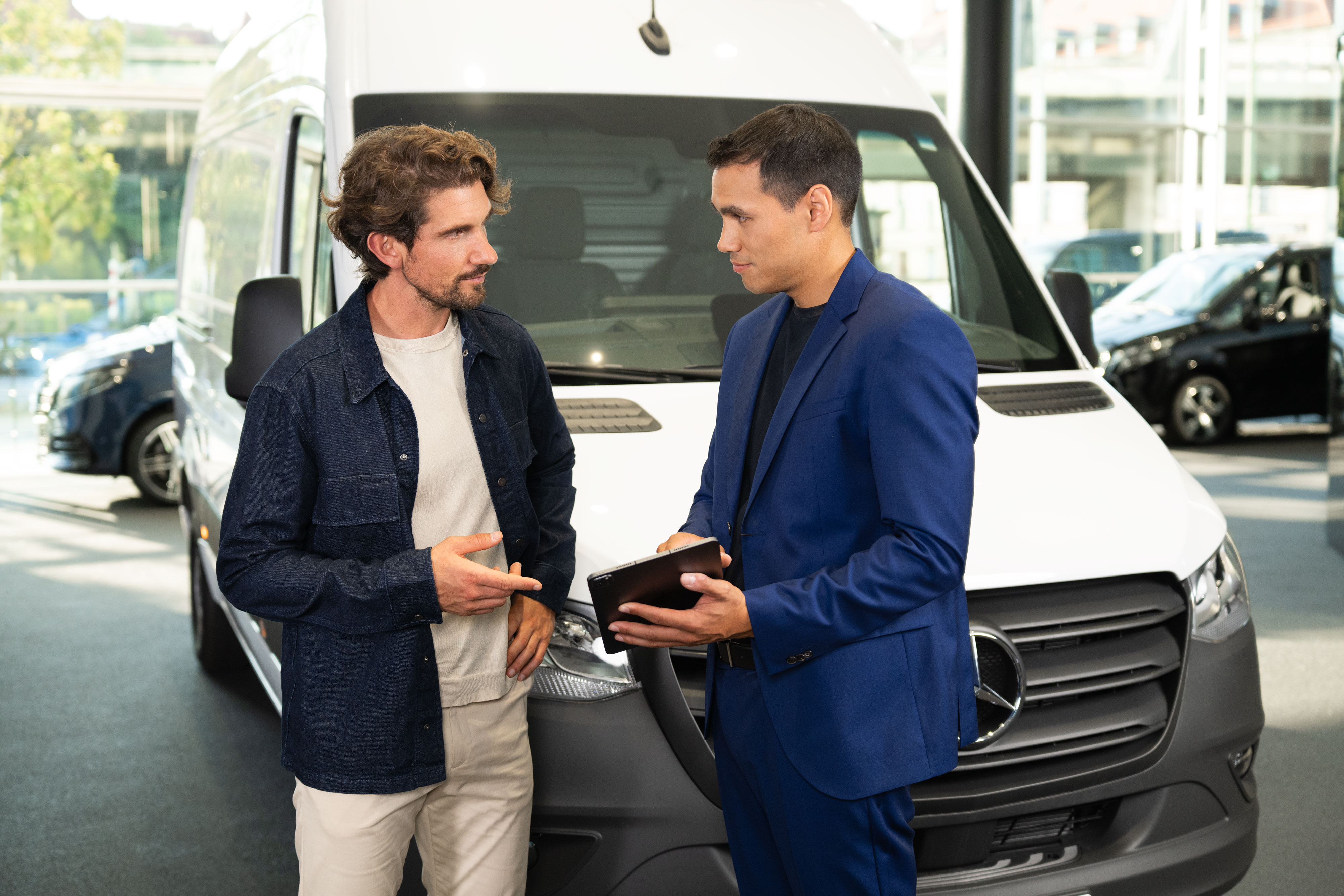 Offerte finanziarie | Mercedes-Benz Due persone che parlano e guardano un dispositivo mobile, in piedi davanti a un furgone Mercedes-Benz.