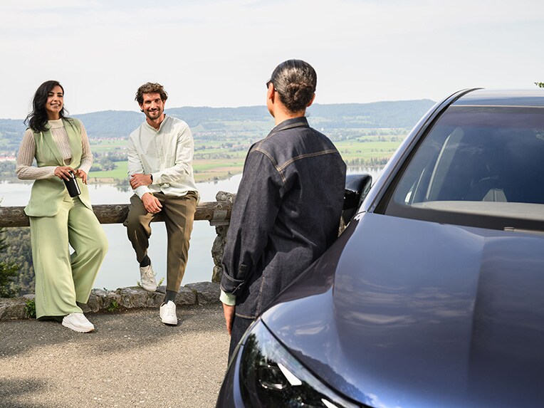 Una persona appoggiata a un veicolo Mercedes-Benz che parla con altre 2 persone appoggiate a una recinzione.