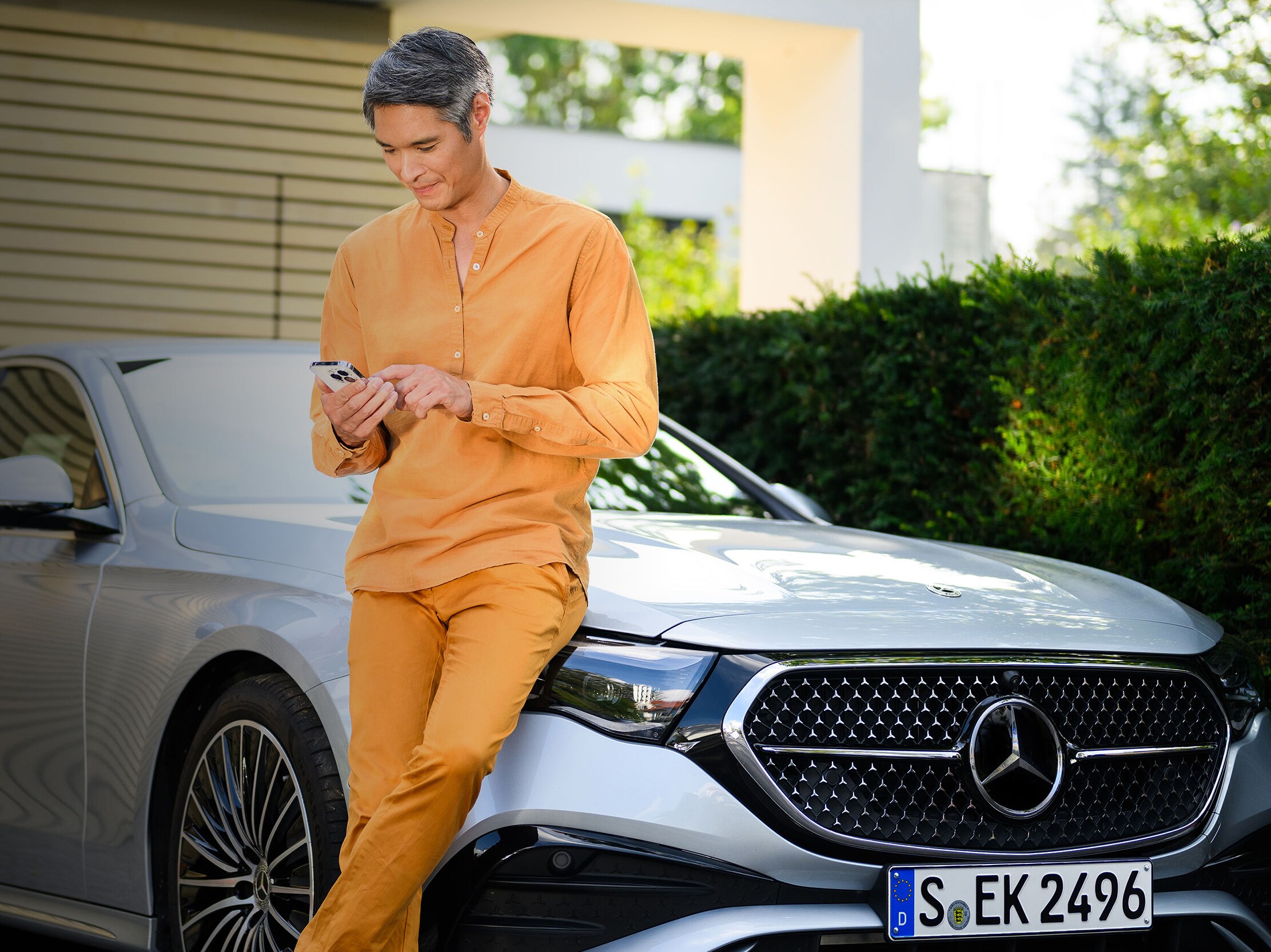 Una persona appoggiata a un veicolo Mercedes-Benz, utilizzando un dispositivo mobile.