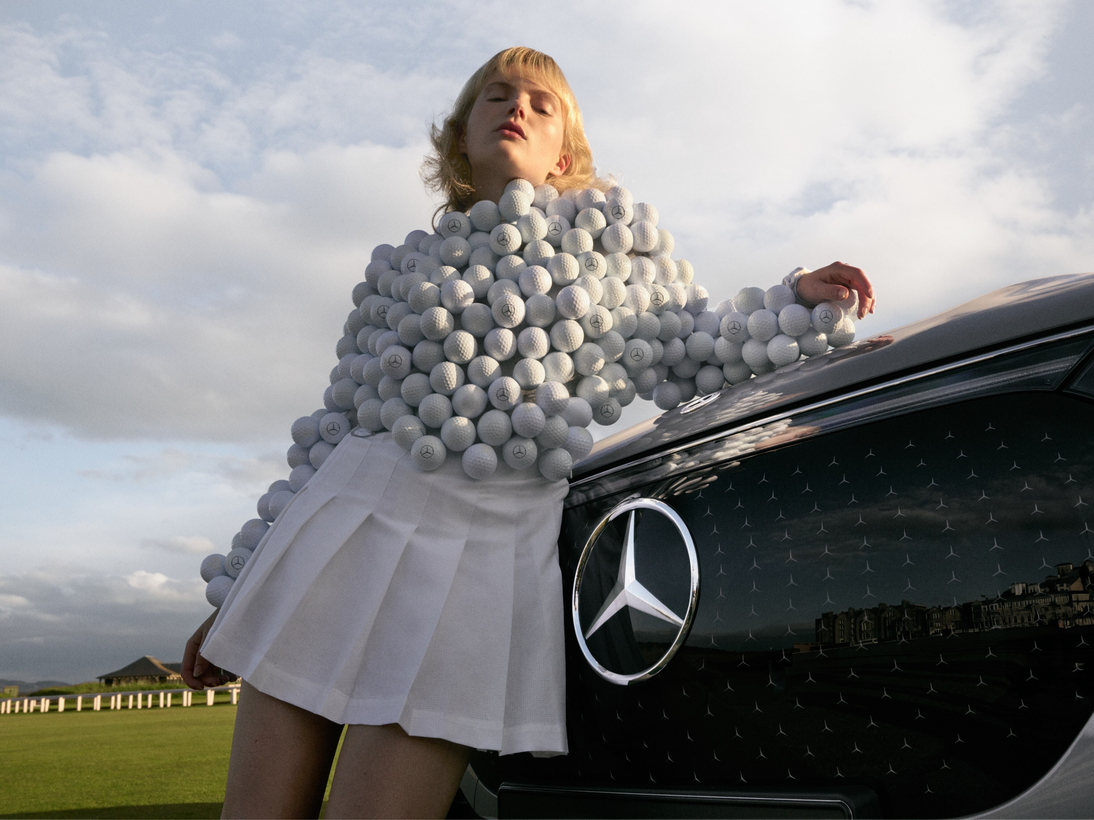 Una donna con una maglia fatta di palline da golf davanti a una Mercedes-Benz EQS SUV